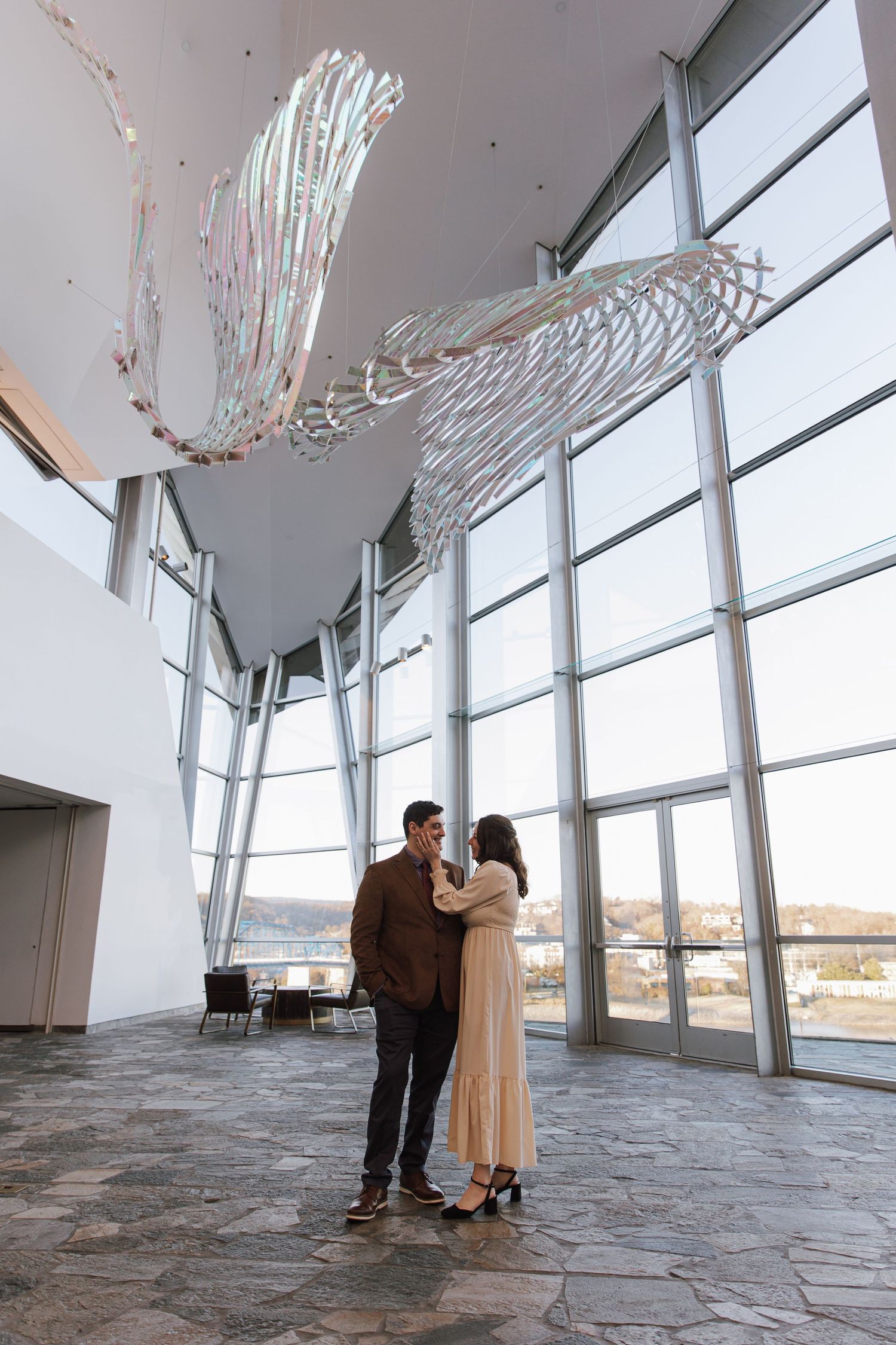 A couple stands together in a modern space with floor-to-ceiling windows.