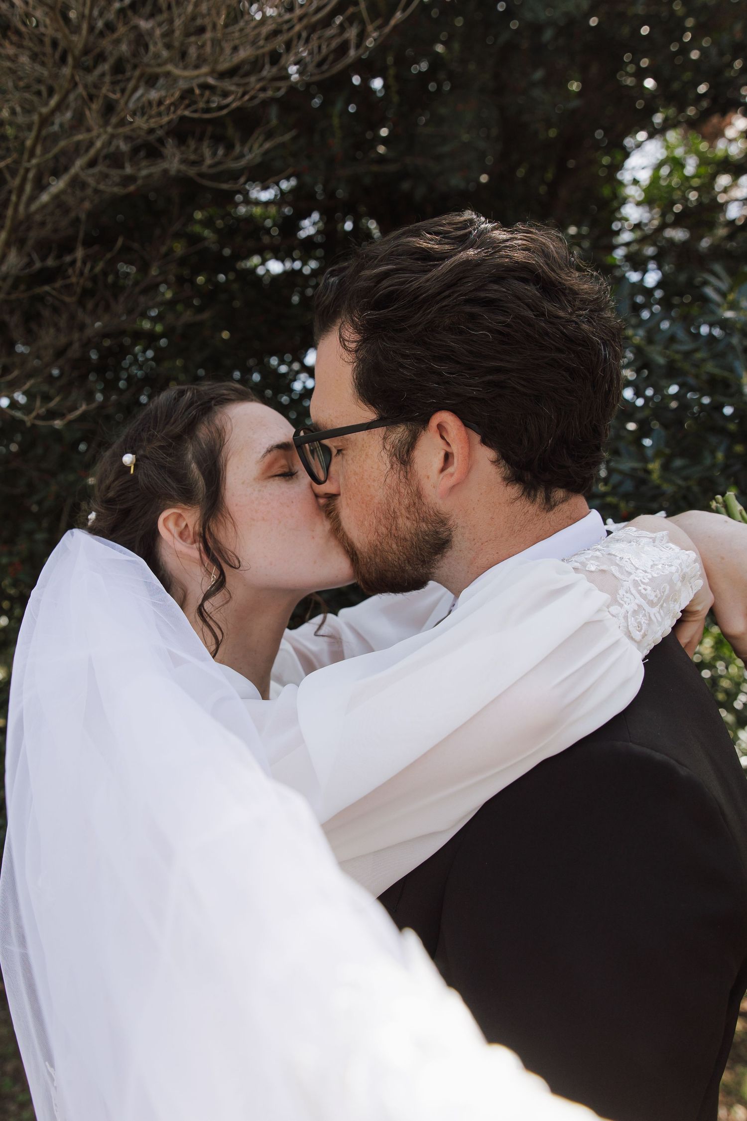 Intimate wedding couple sharing a kiss outdoors against greenery.