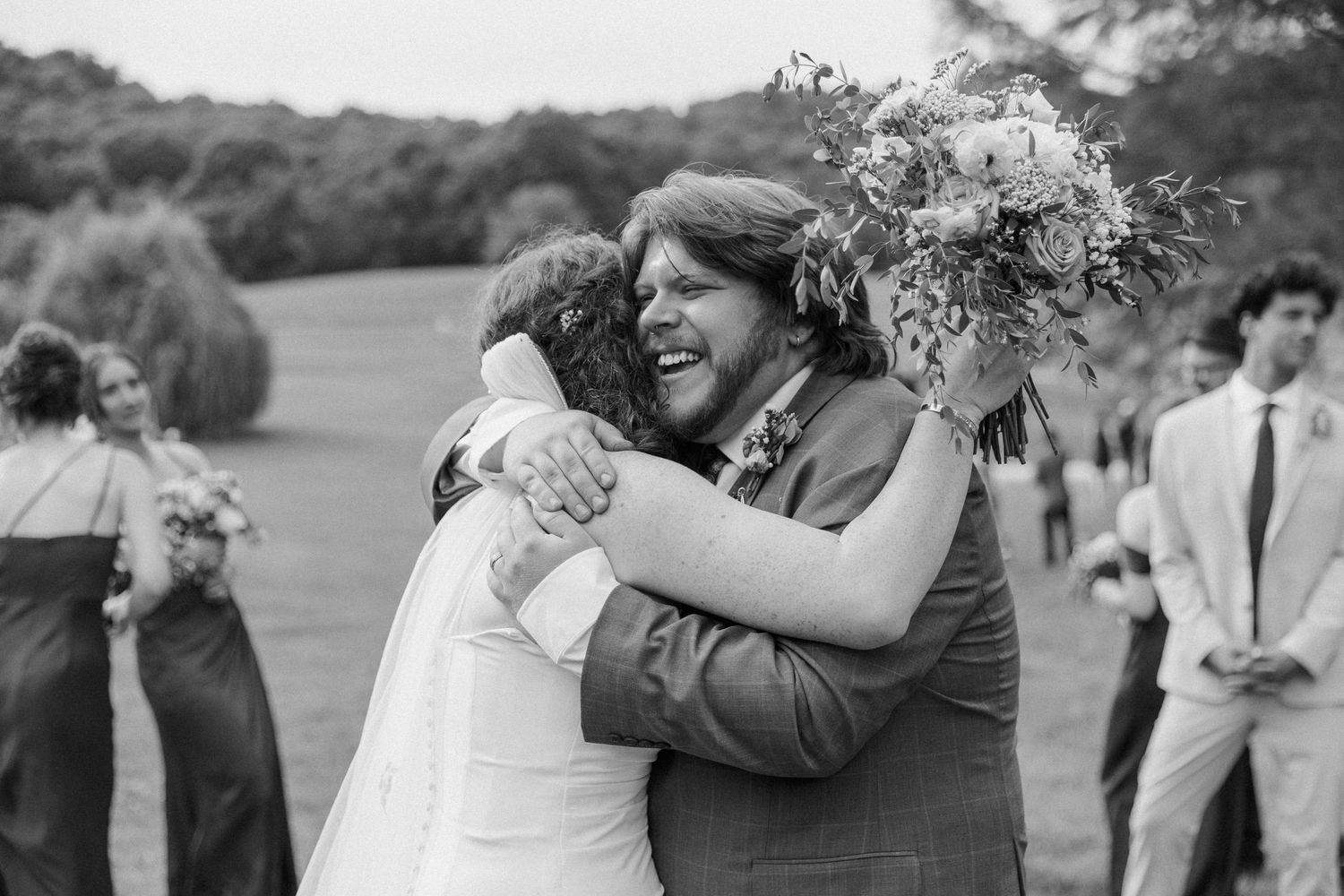 Black and white photo of a joyful bride and groom embracing at their outdoor wedding ceremony.