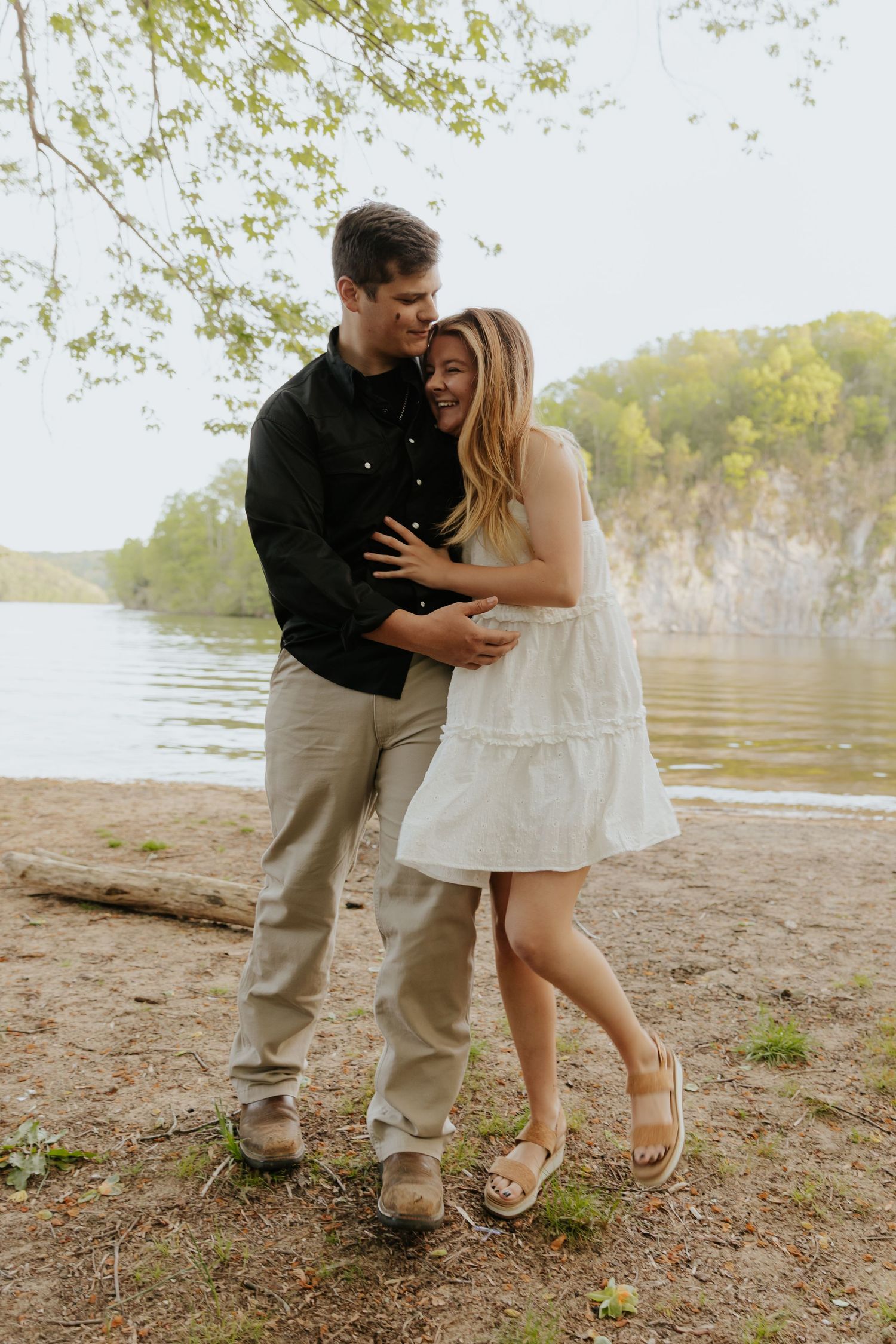 A couple embraces lovingly by a scenic riverbank during a romantic outdoor photo session.