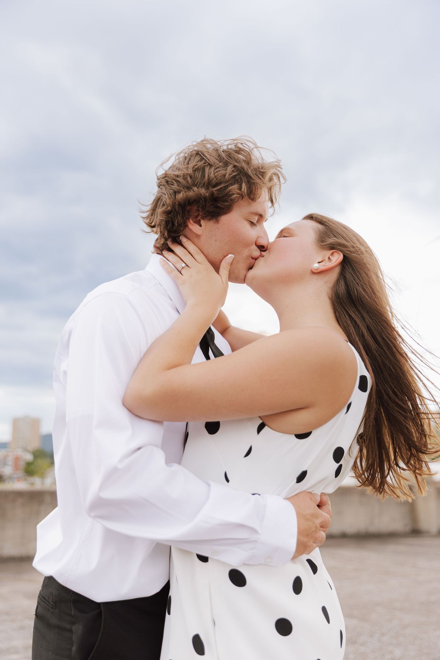 A couple in polka dot dress and white shirt share a romantic moment on a rooftop.