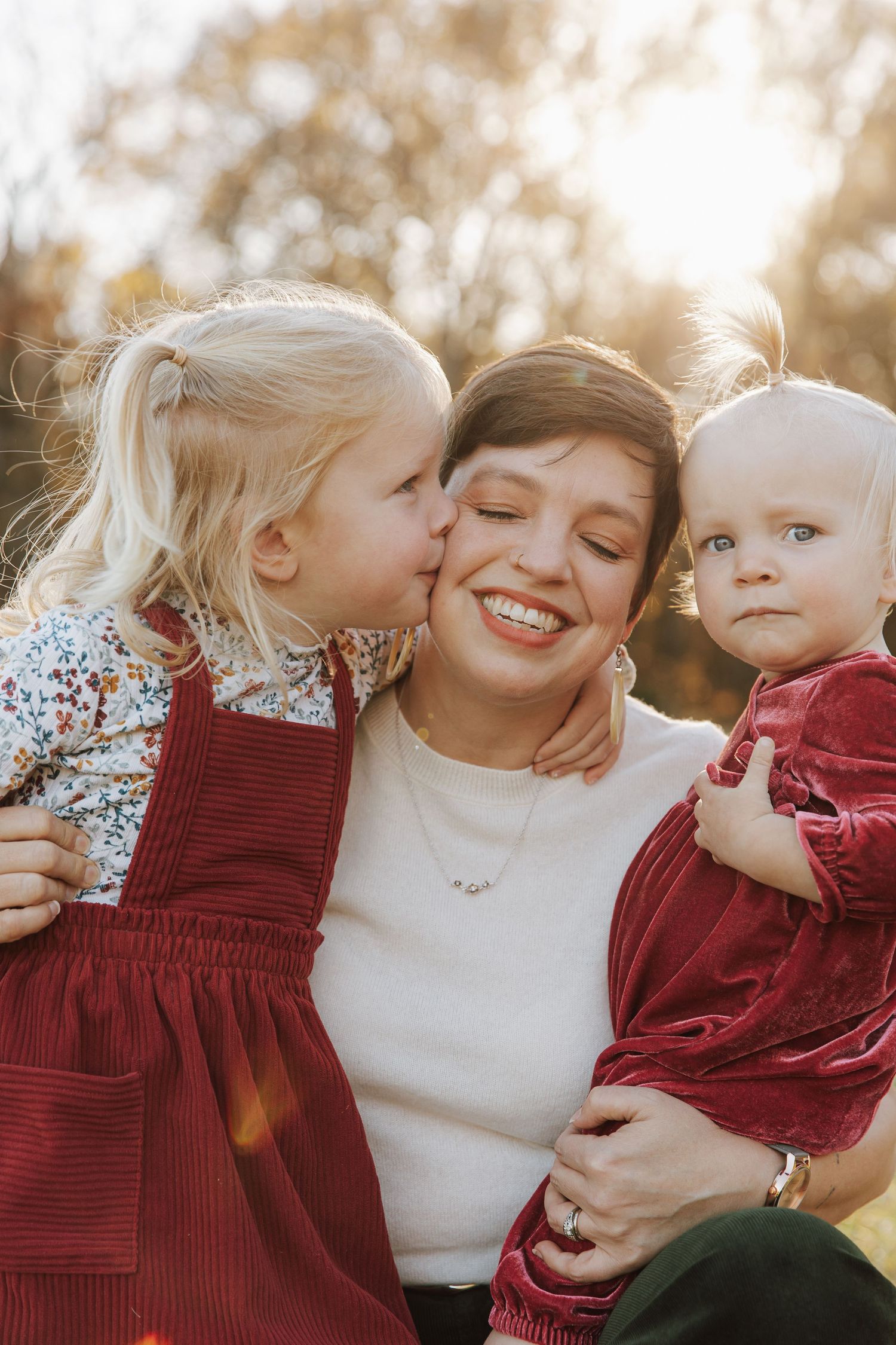 A tender family moment captured outdoors with warm autumn lighting and coordinating burgundy outfits.