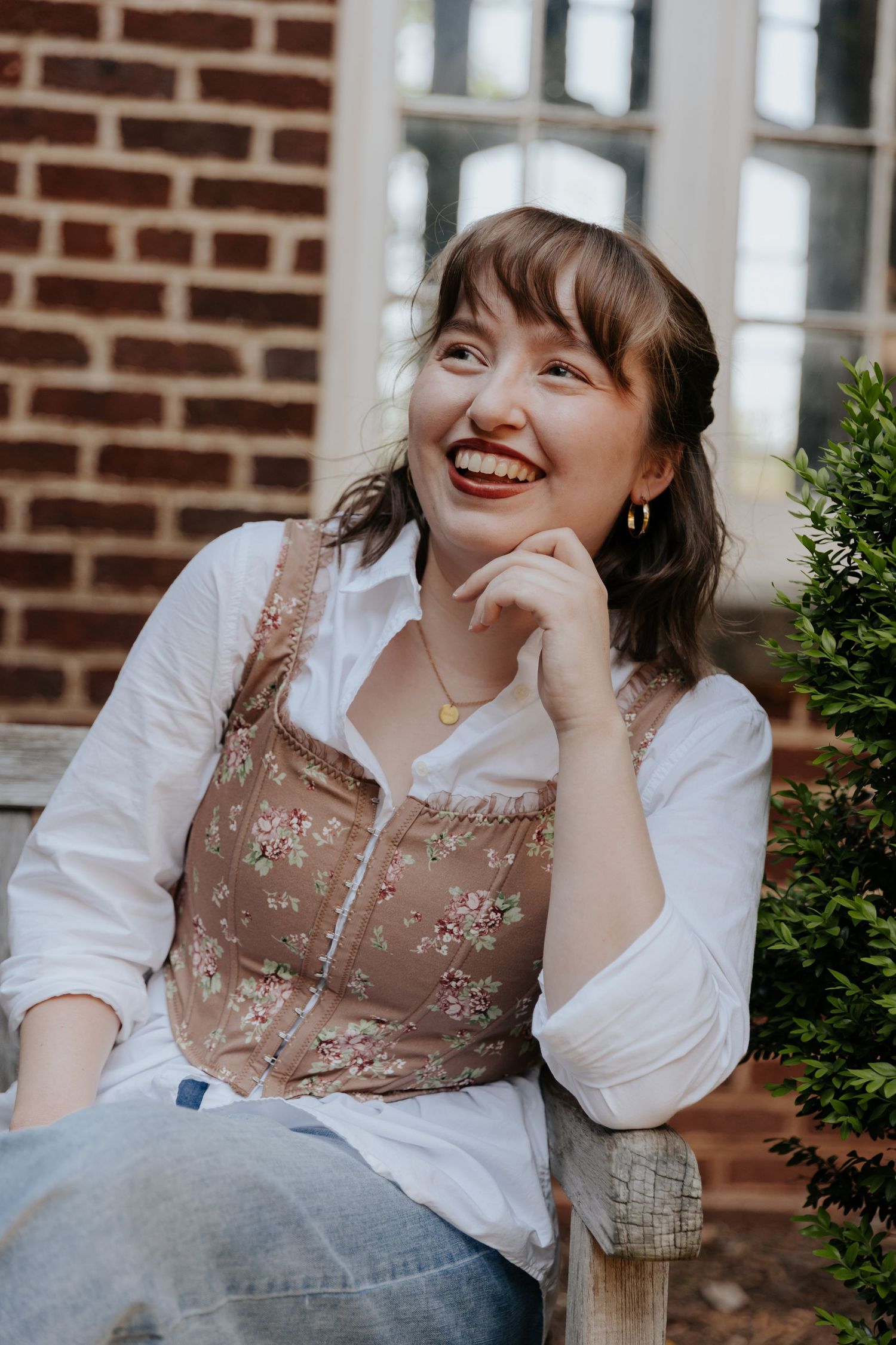 A series of candid portraits showing someone in a white blouse and embroidered brown vest sitting by a brick wall.