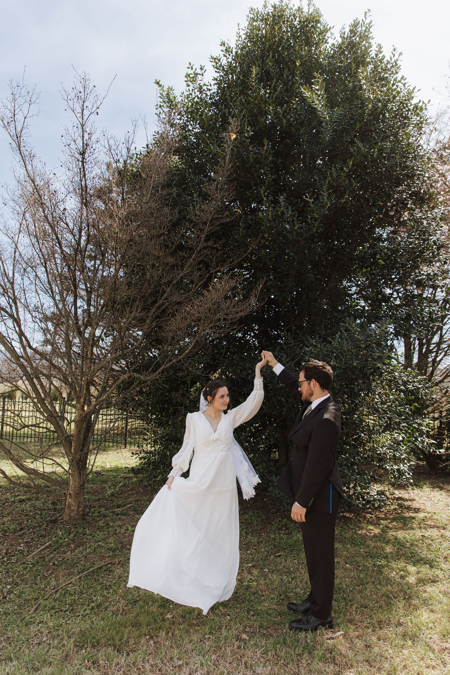 Playful wedding couple dancing and twirling in an outdoor garden setting.