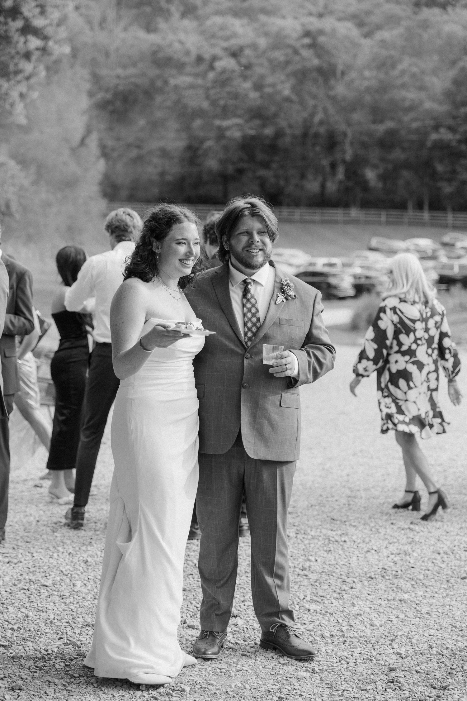 Bride in white gown and groom in suit smiling together at outdoor wedding reception.