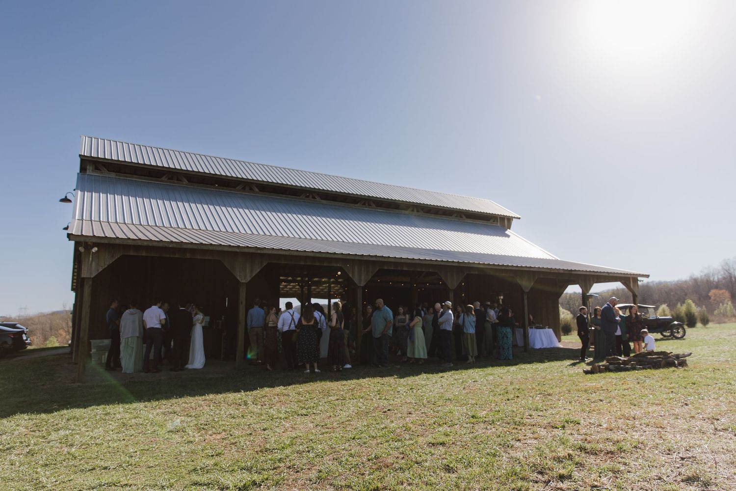 Guests gather outside a rustic wooden barn venue on a sunny day for an outdoor country wedding celebration.