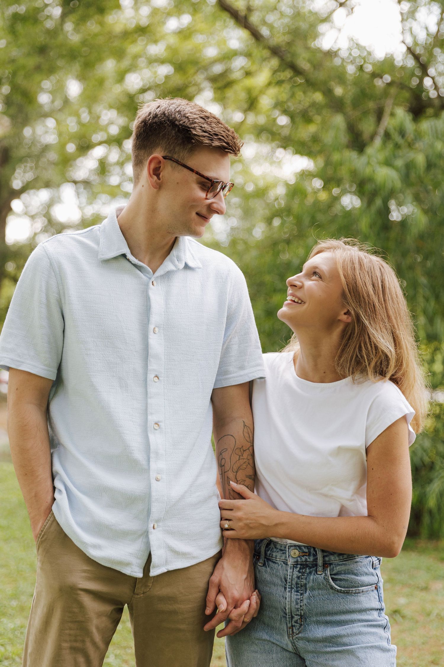 A couple shares a loving glance while holding hands in a park setting.