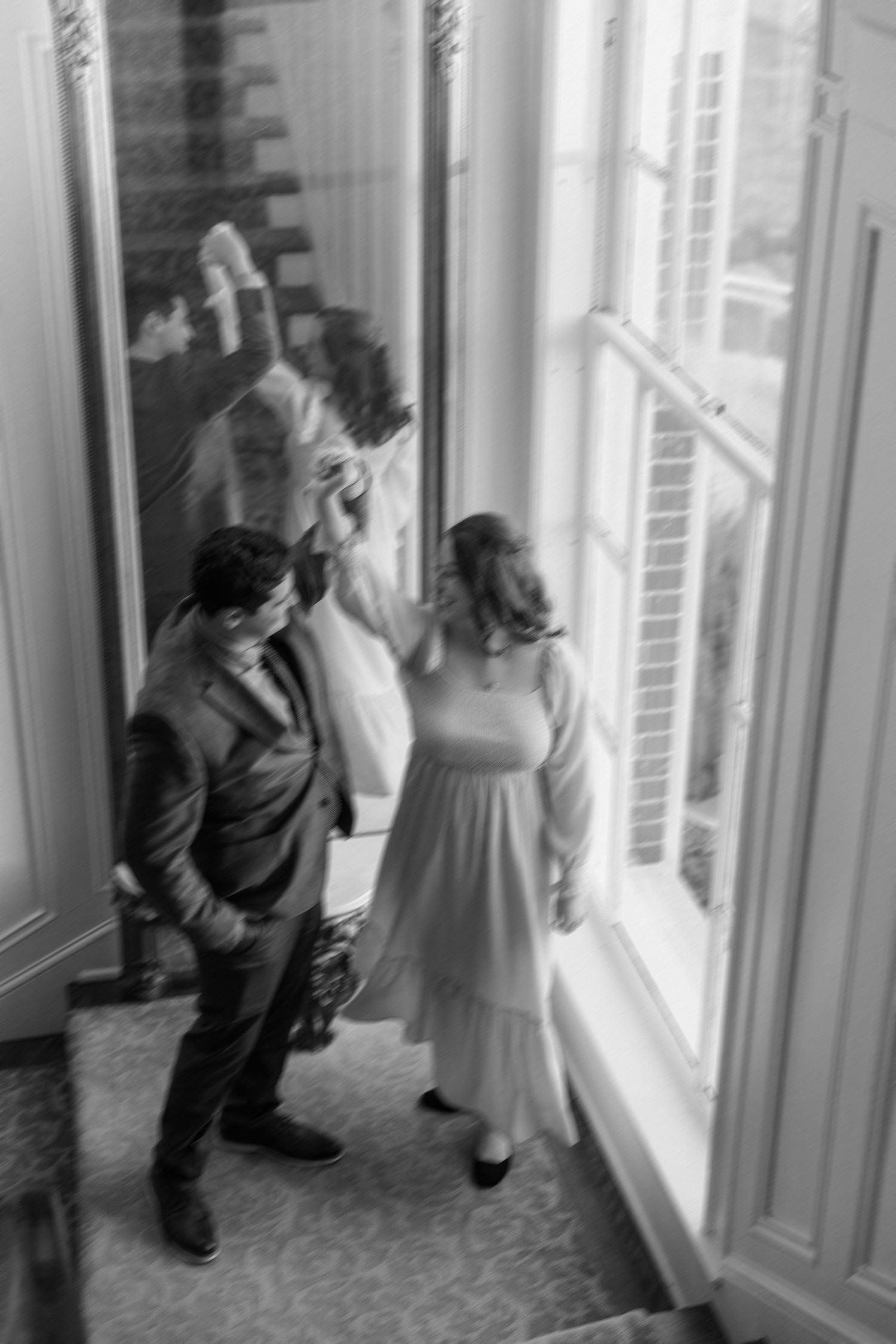 A black and white photo of people looking out tall windows in formal attire.