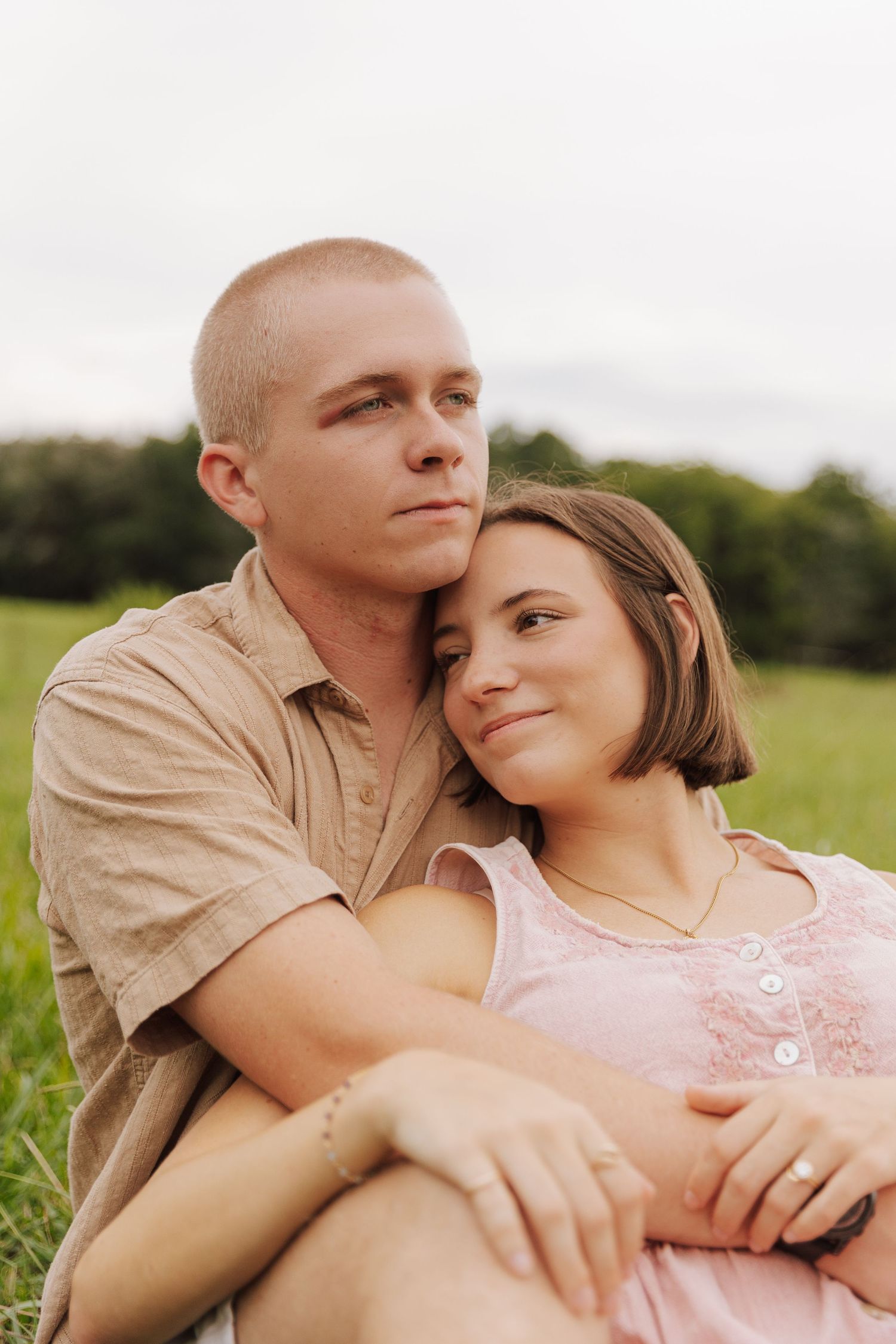Romantic couple embraces in a sunlit meadow wearing matching beige and pink outfits.