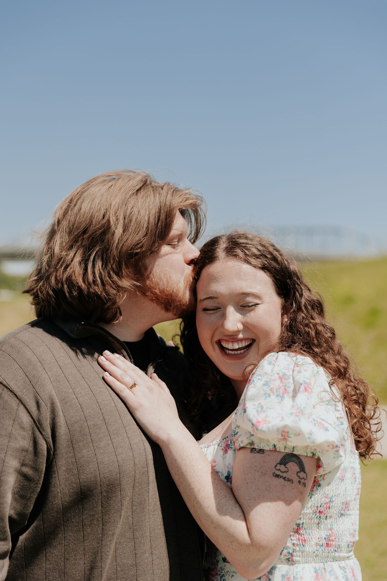 A tender moment shared between a couple outdoors on a sunny day, with one person wearing a floral dress and the other in brown.