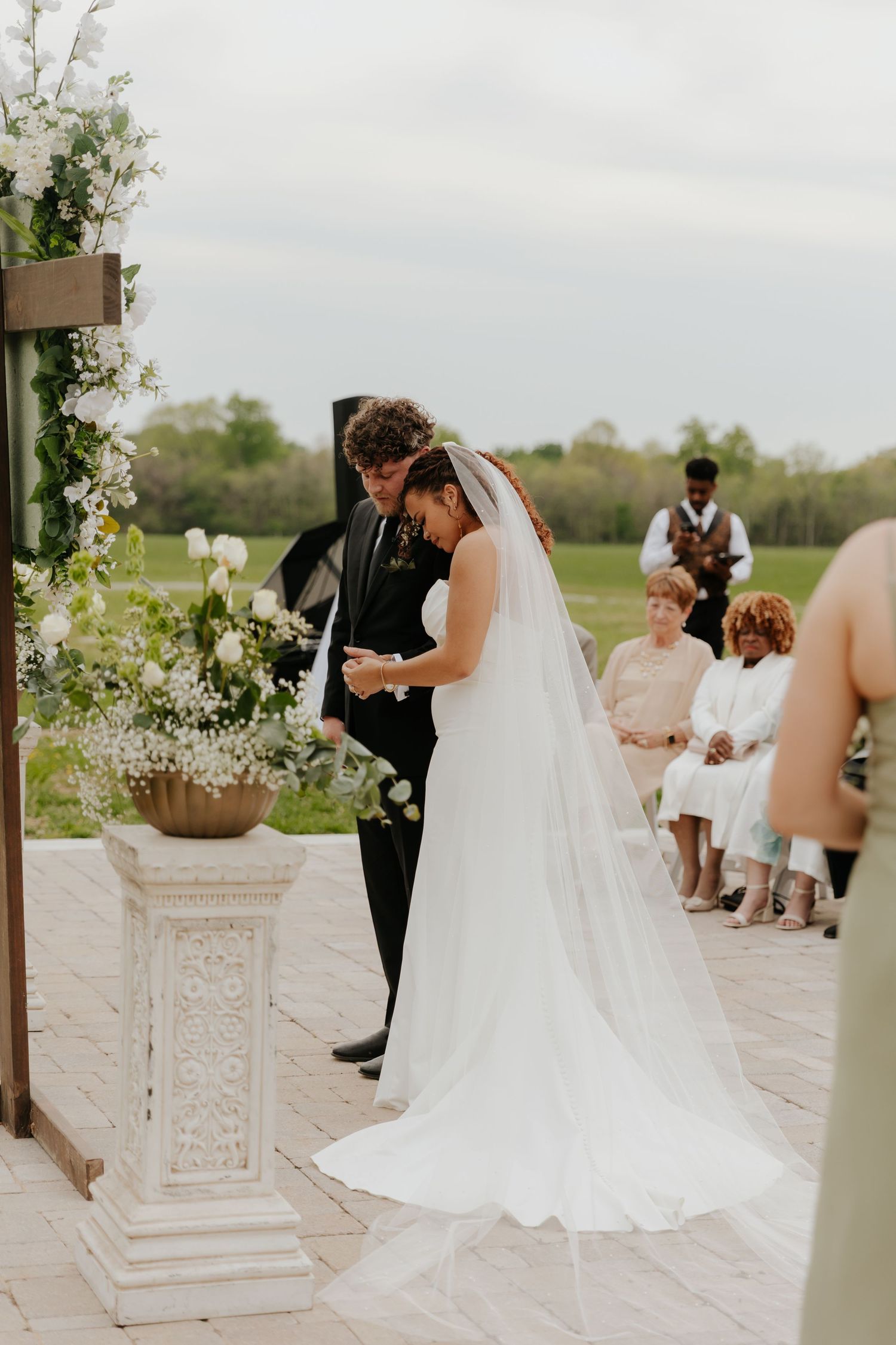 Outdoor wedding ceremony with decorative white pillars and floral arrangements.