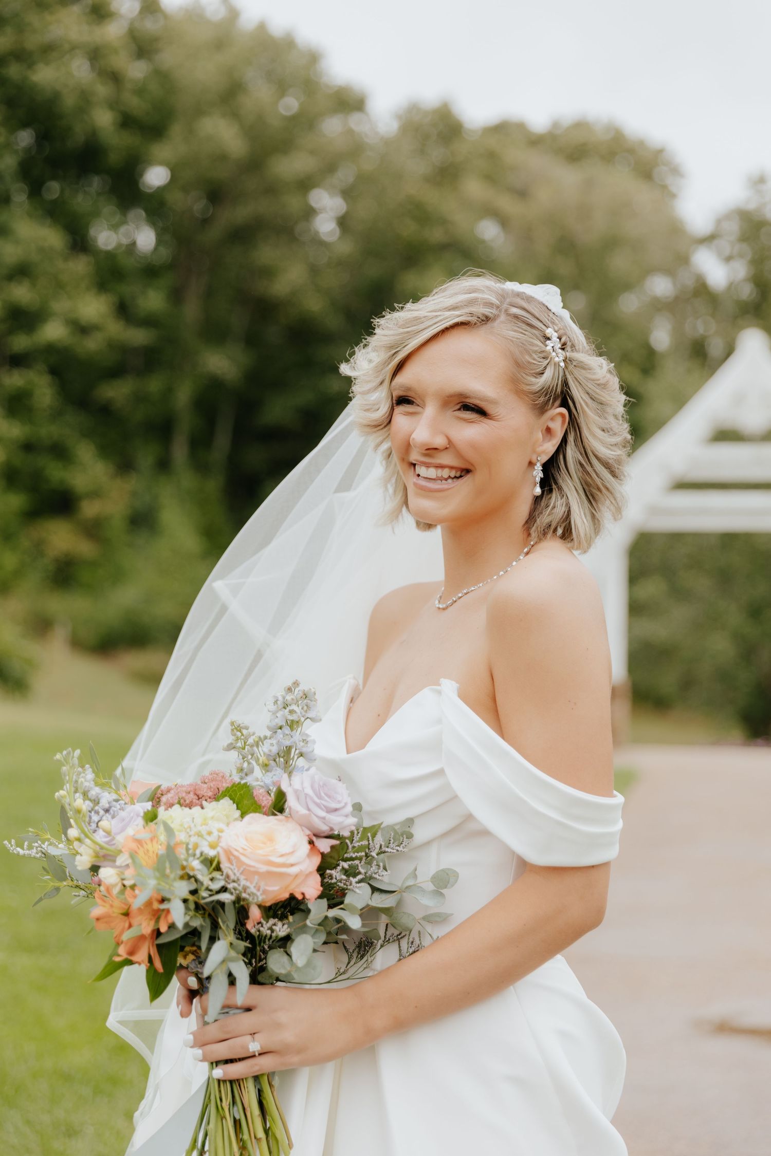 Bride with bouquet of peach and white flowers posing in garden setting.