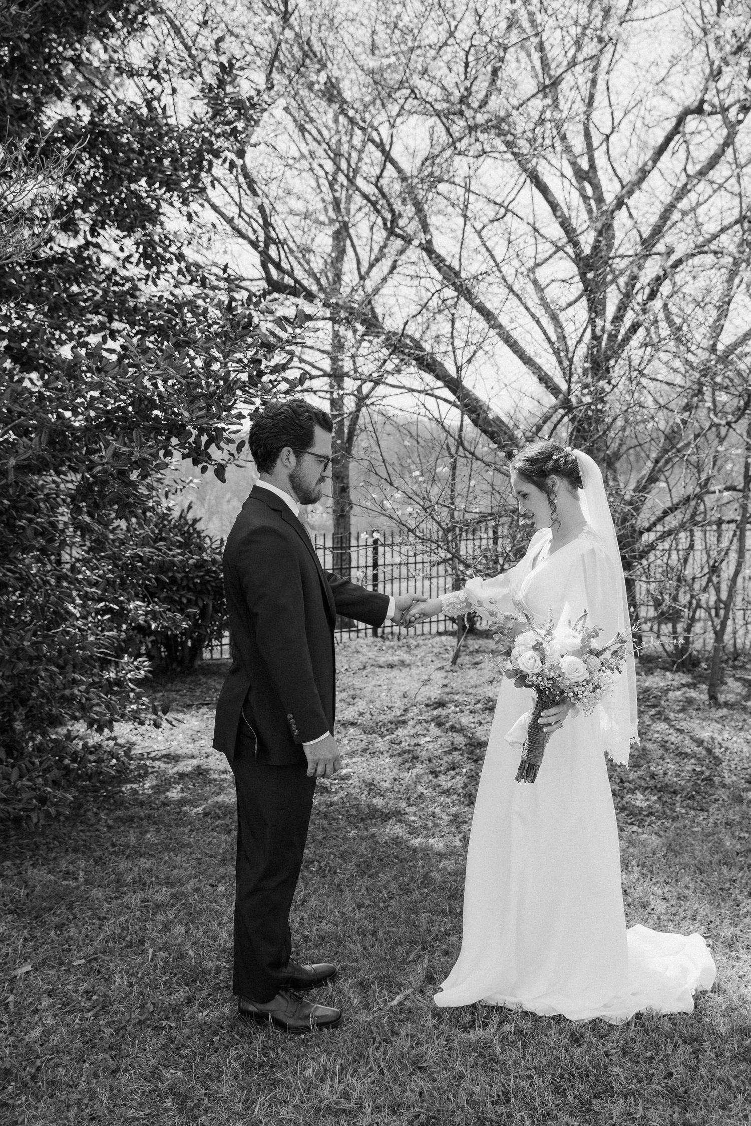 Black and white photo of groom holding bride's hand during outdoor first look moment.