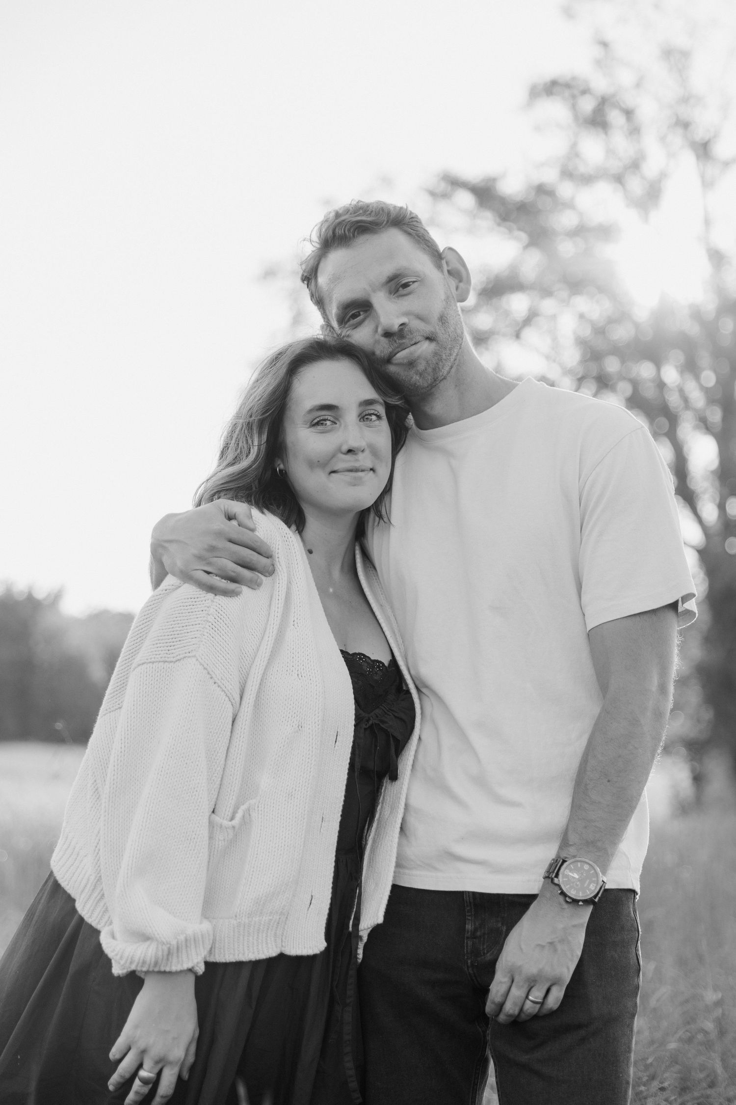 A couple embraces outdoors in a romantic black and white photo.