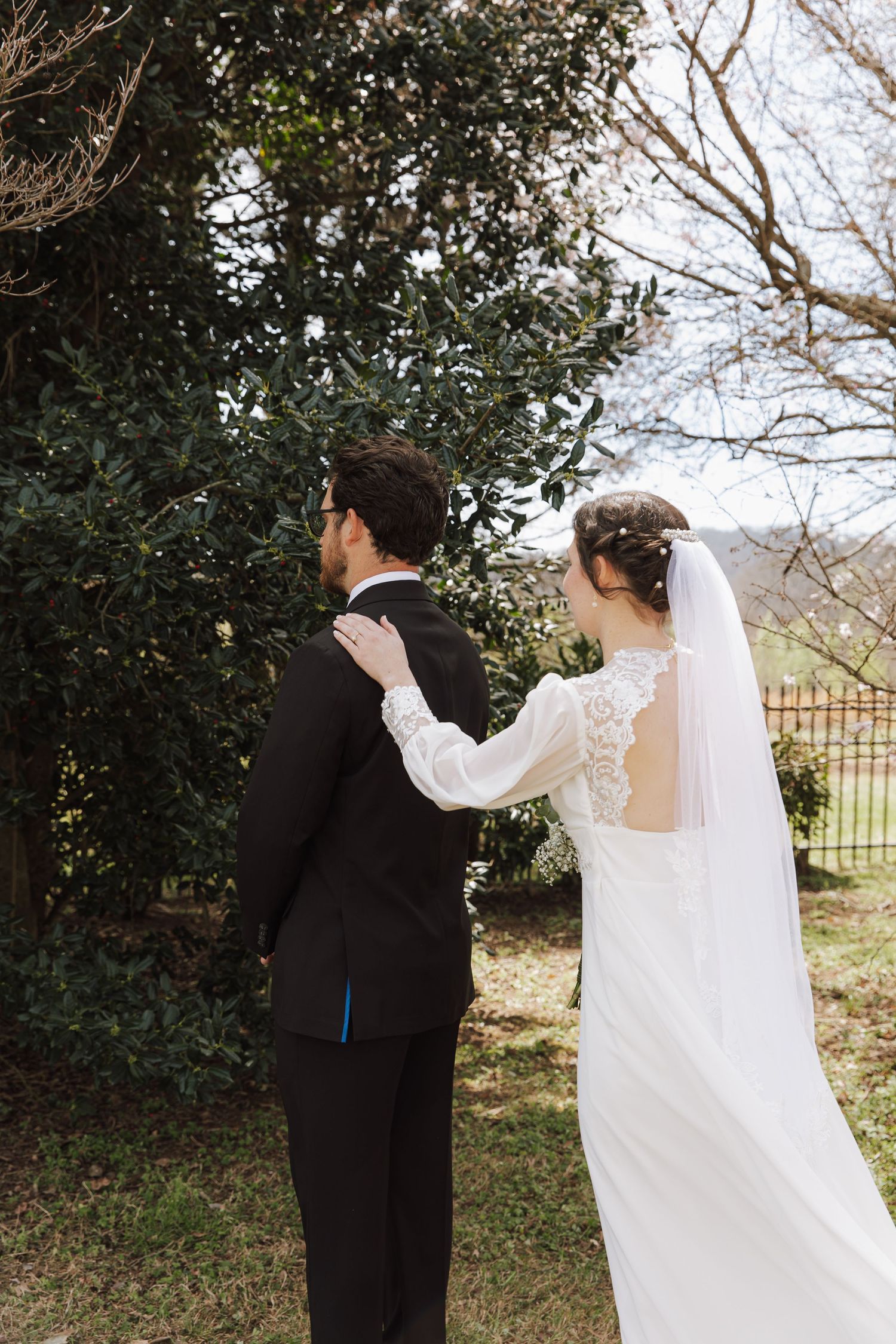 Bride and groom walking together outdoors, bride in lace back wedding dress with veil.