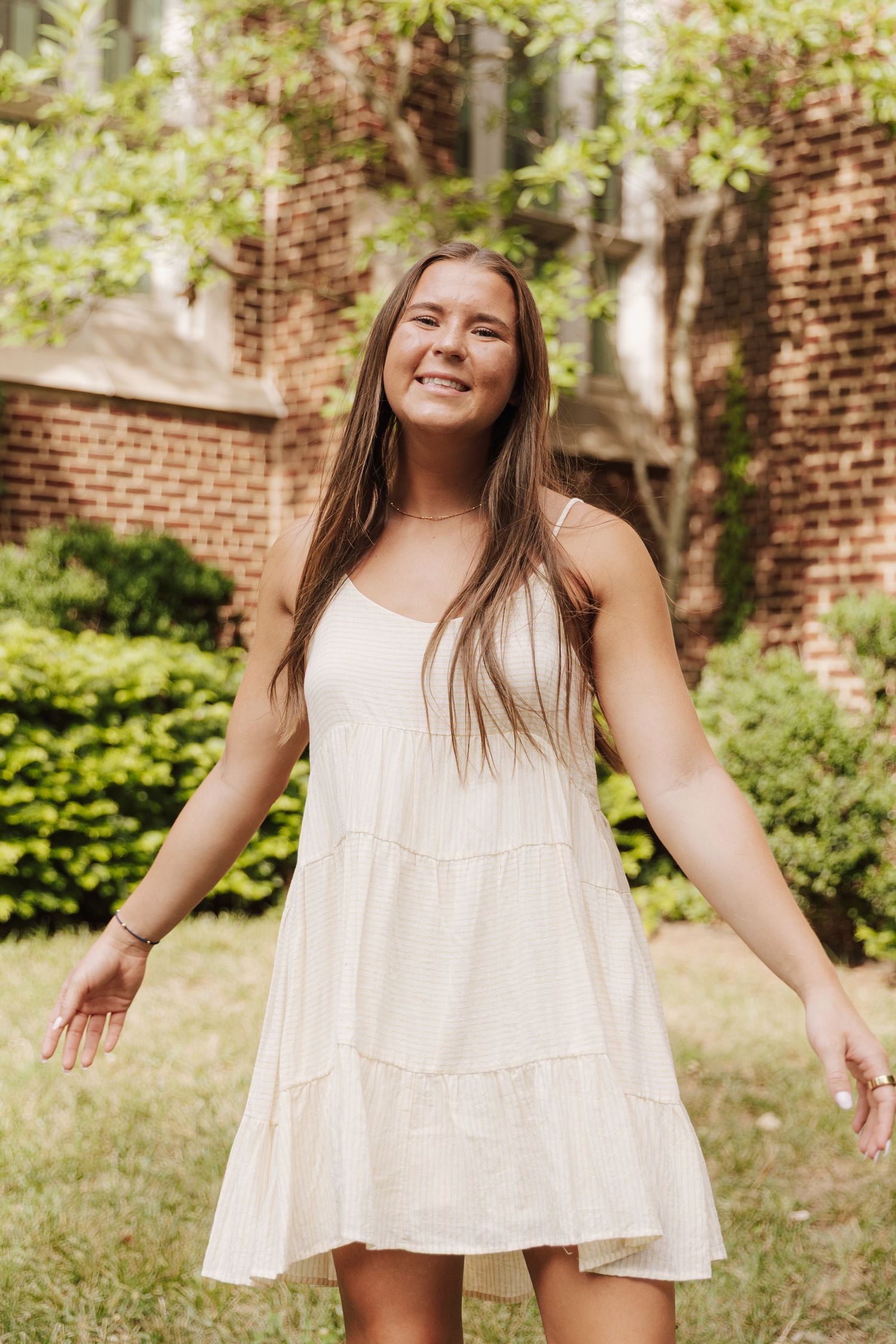 A series of outdoor portraits showing someone in a flowing white summer dress against a brick wall and garden background.