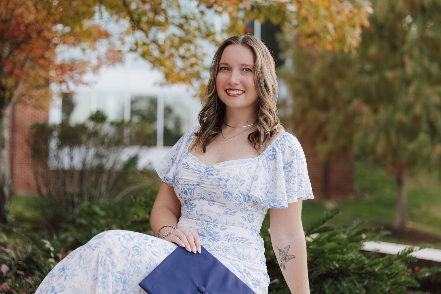 A woman in a blue floral dress poses outdoors during autumn.