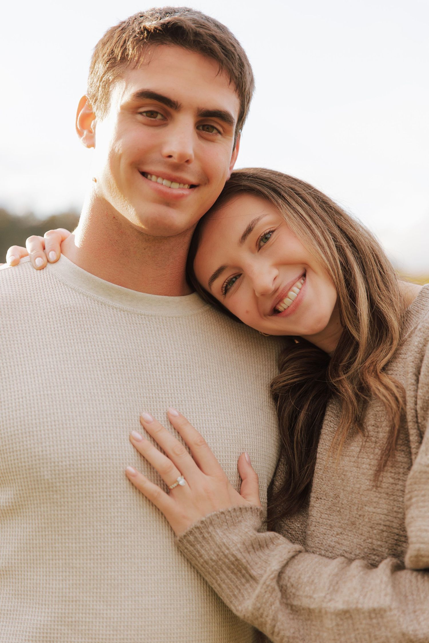 Couple in neutral sweaters shares loving embraces in warm sunlight.