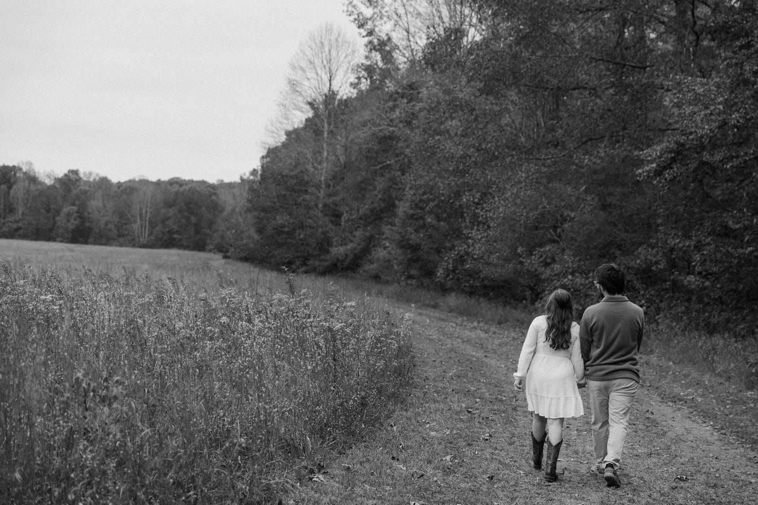 People walking along a winding dirt path through a wooded area on a sunny day.