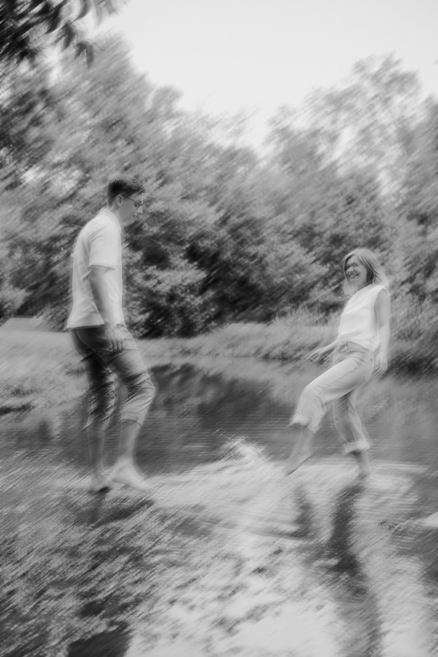 A blurred black and white photo of two people standing on rocks by water.