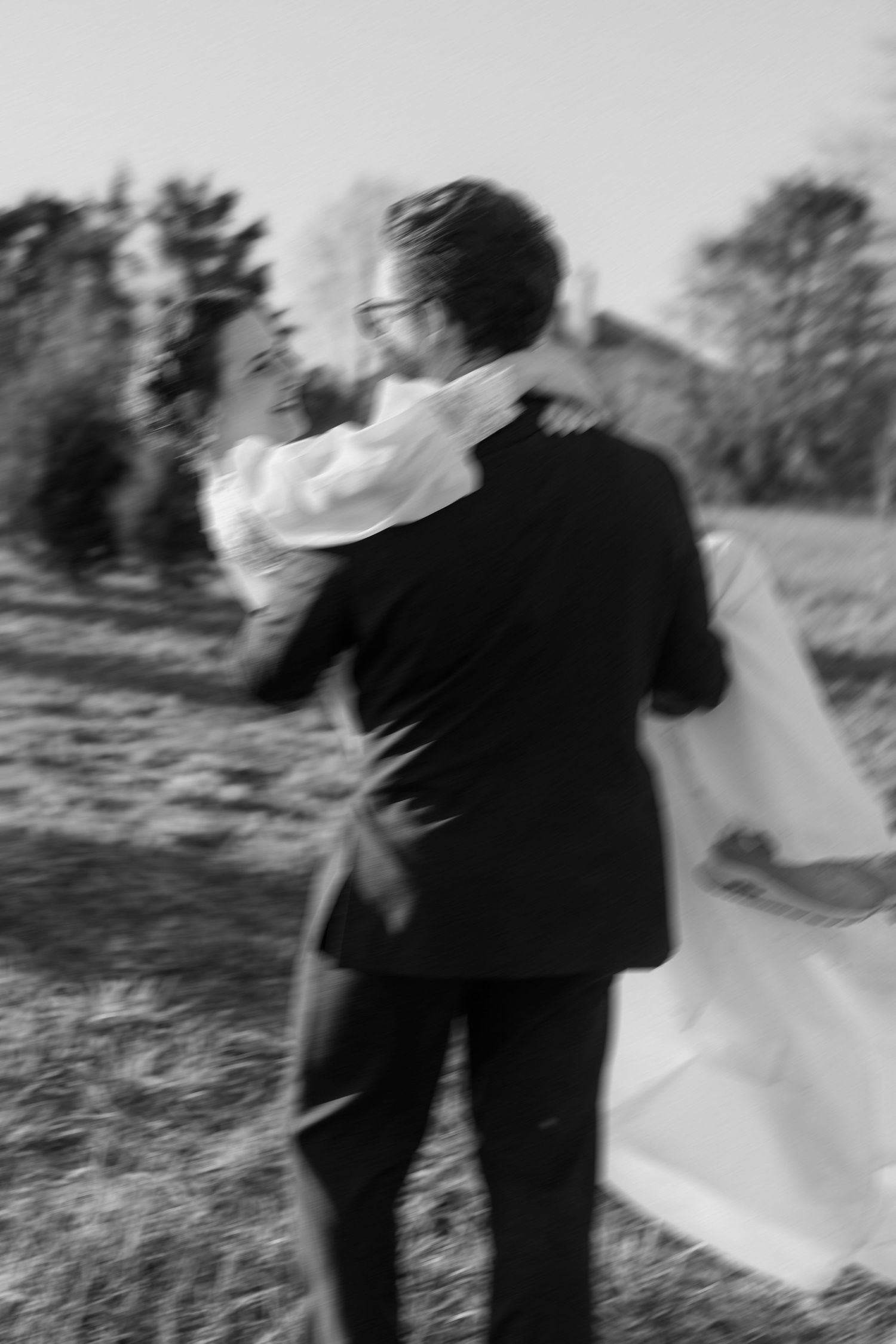 Blurred artistic black and white photo of bride and groom embracing outdoors after wedding.