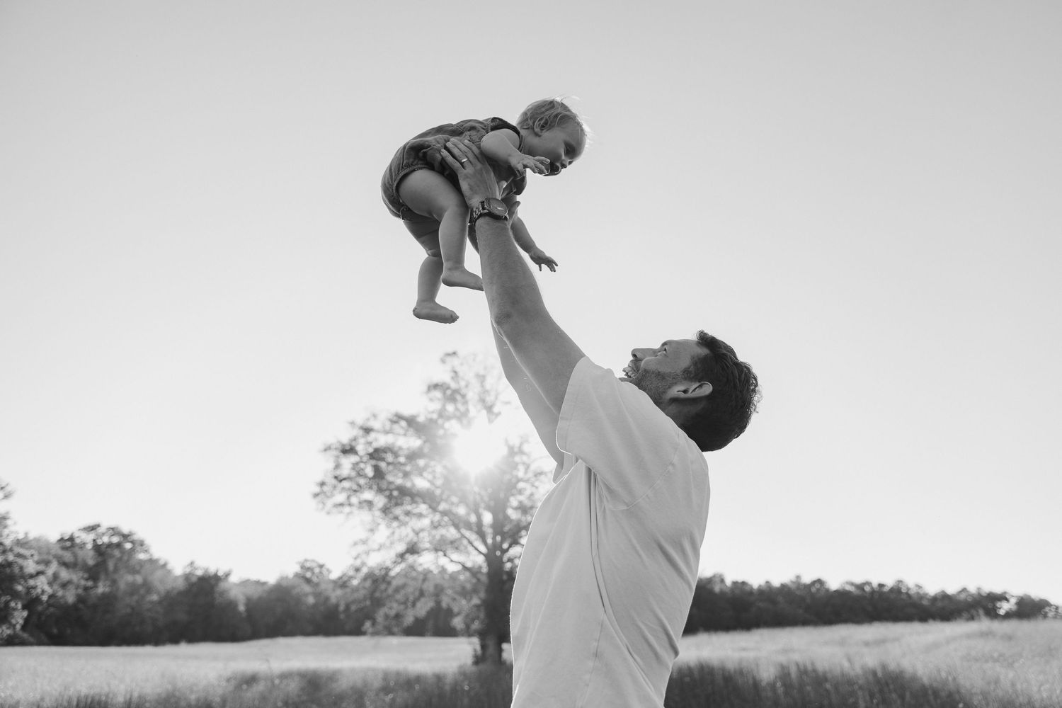 A dad tossing his young daughter in the air as she laughs.