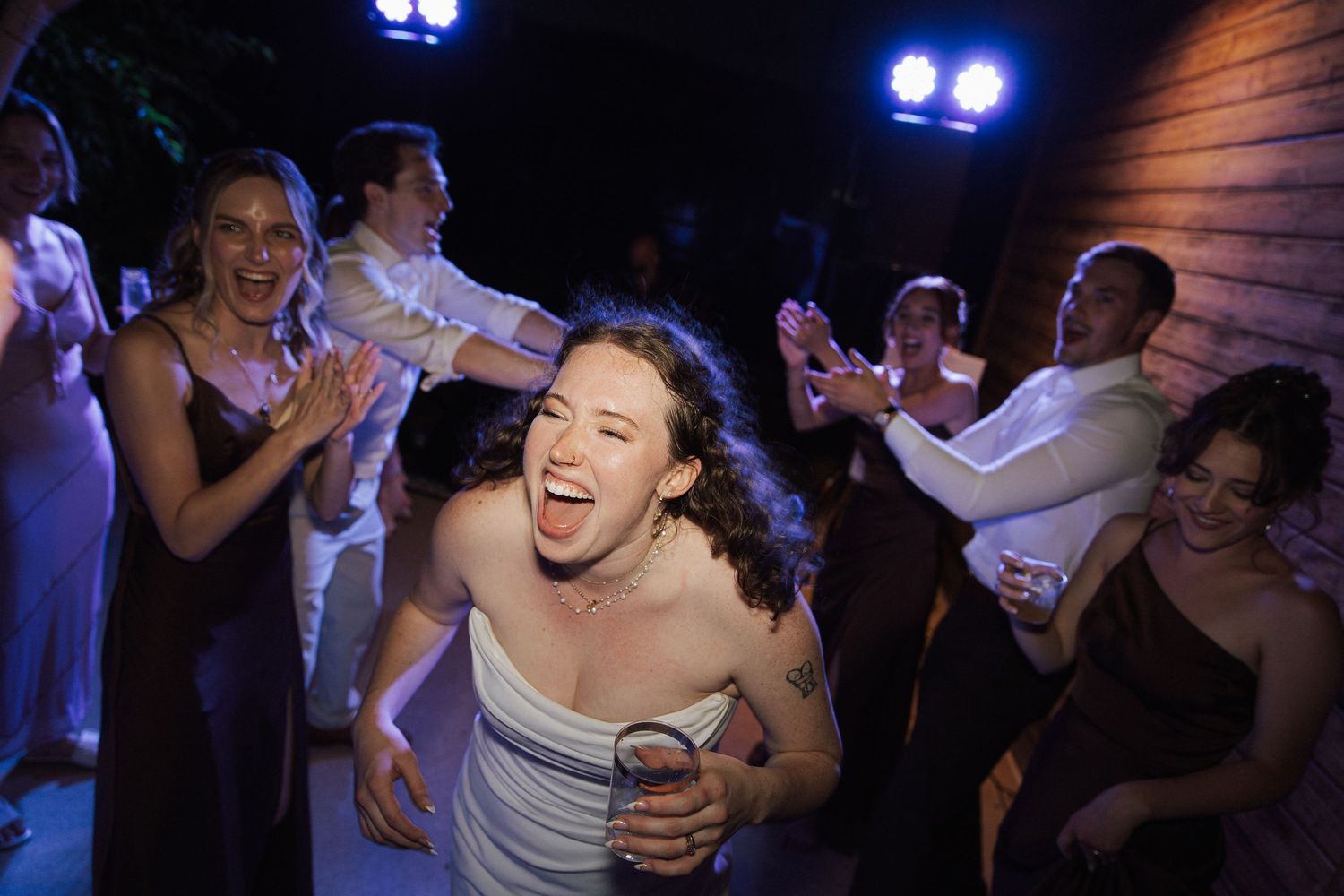 Joyful bride laughing and dancing with guests at a lively wedding reception party.