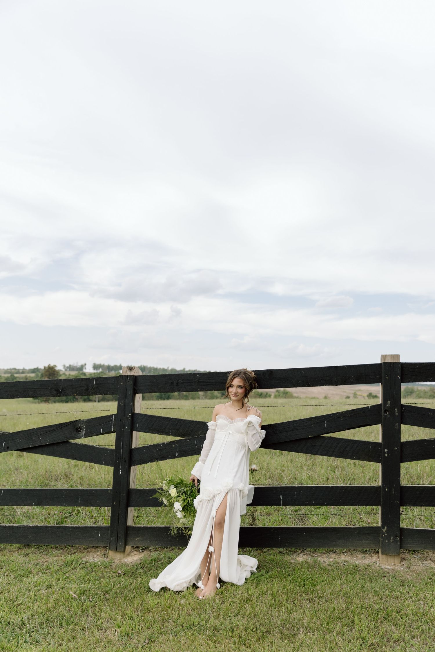 Bride elegantly against black fence in a Tennessee countryside setting with a long flowy dress on.