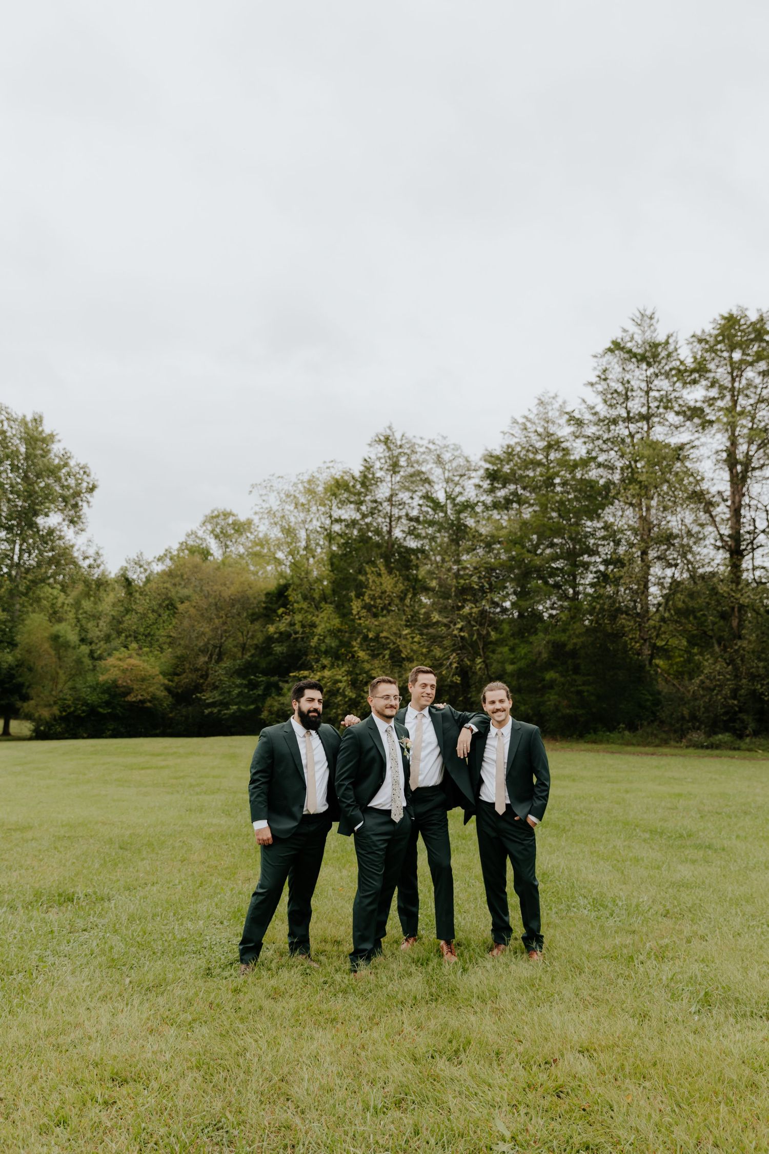 Groomsmen in black suits standing together in green field.