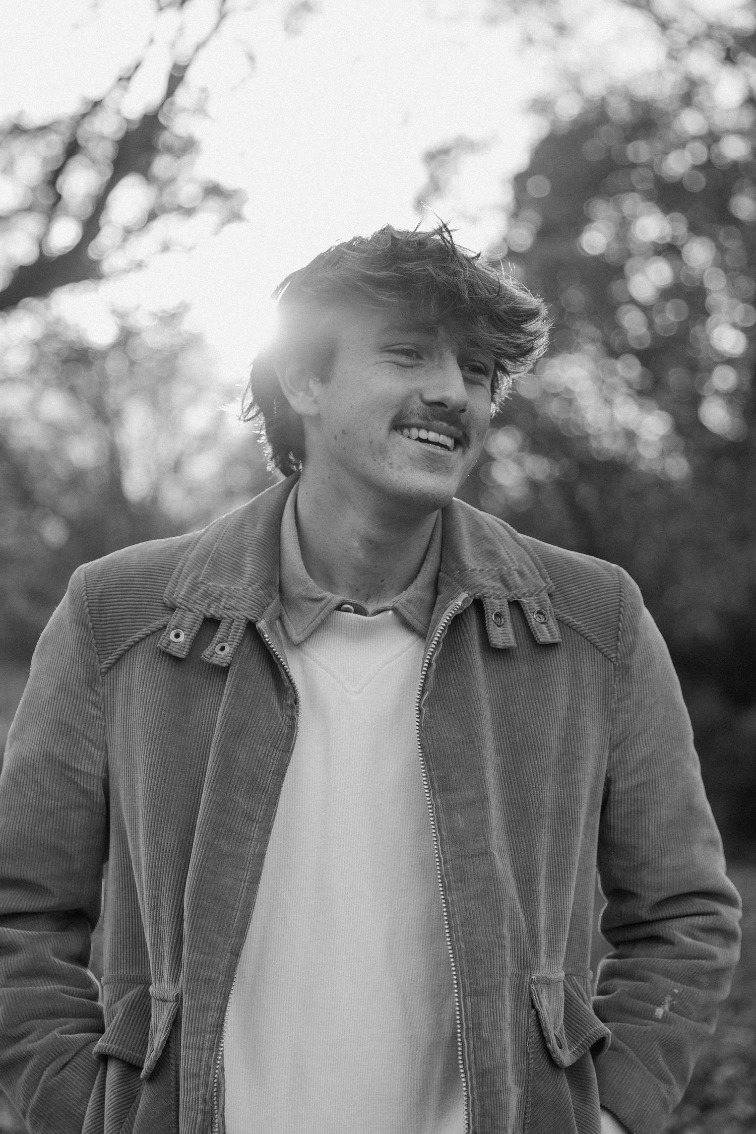 Black and white portrait of someone in a casual jacket smiling outdoors with bokeh lighting effects.