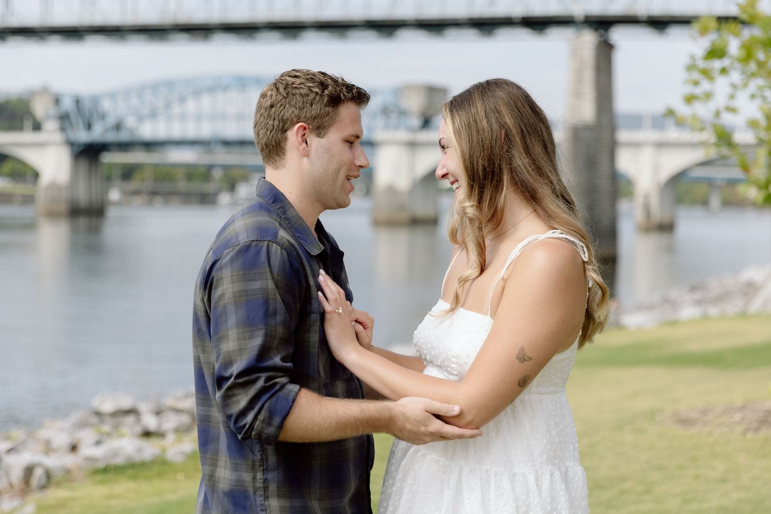 A romantic couple in casual and white dress attire share tender moments in a wooded outdoor setting.
