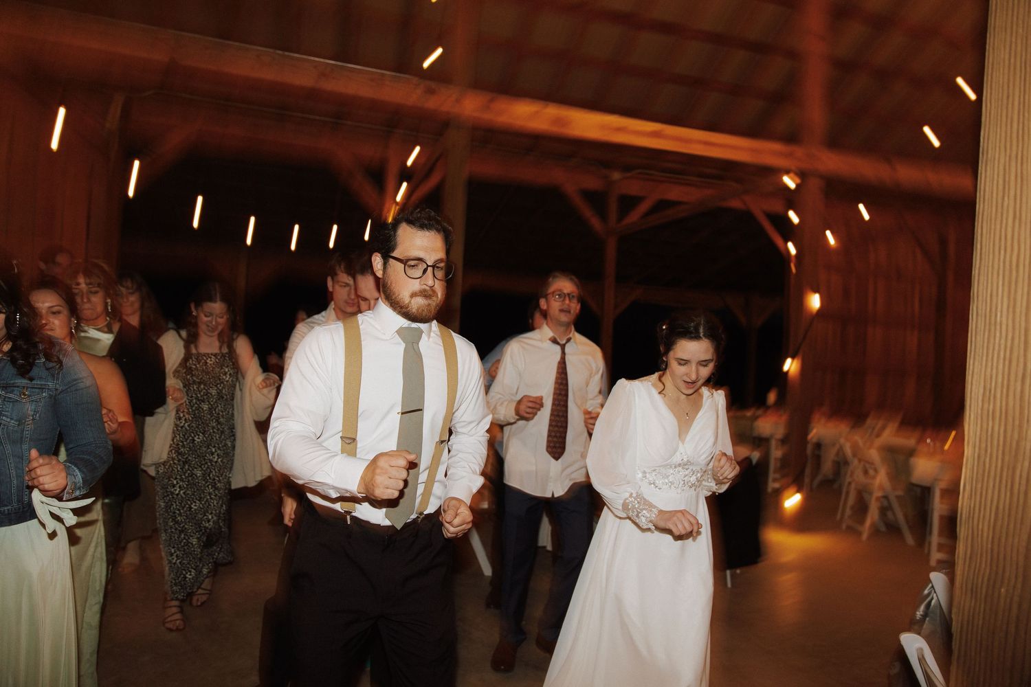 Bride and groom dancing together at rustic barn wedding reception with warm string lights.