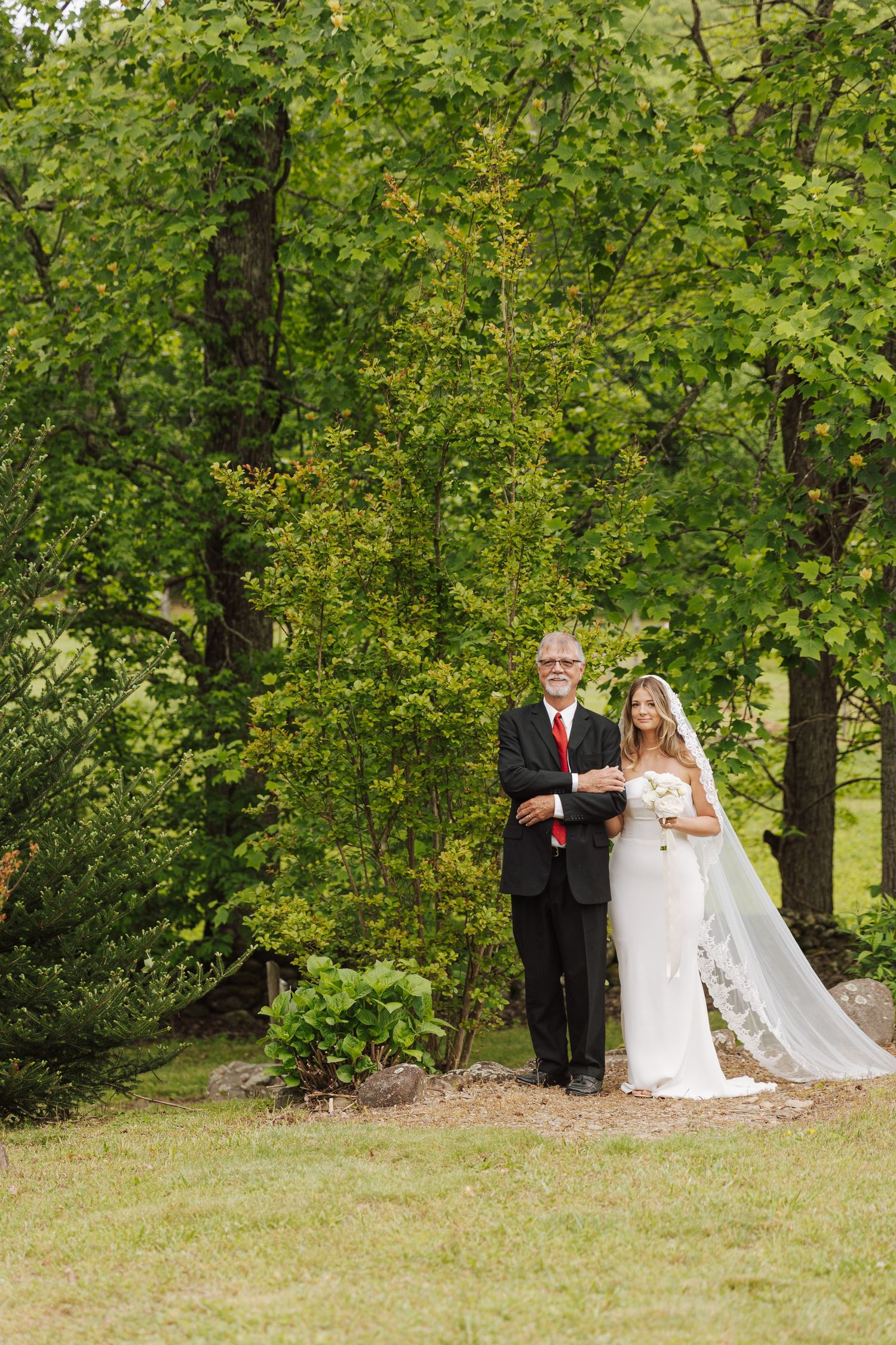 A wedding ceremony scene in a lush green outdoor setting with trees in the background.