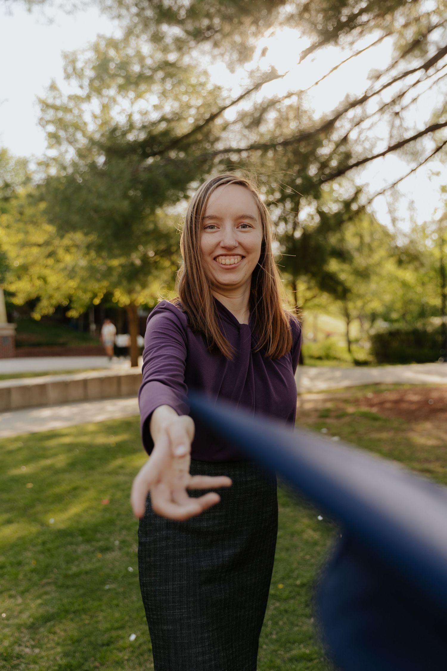A person in a purple sweater smiles and reaches towards the camera in a series of four connected outdoor photos.