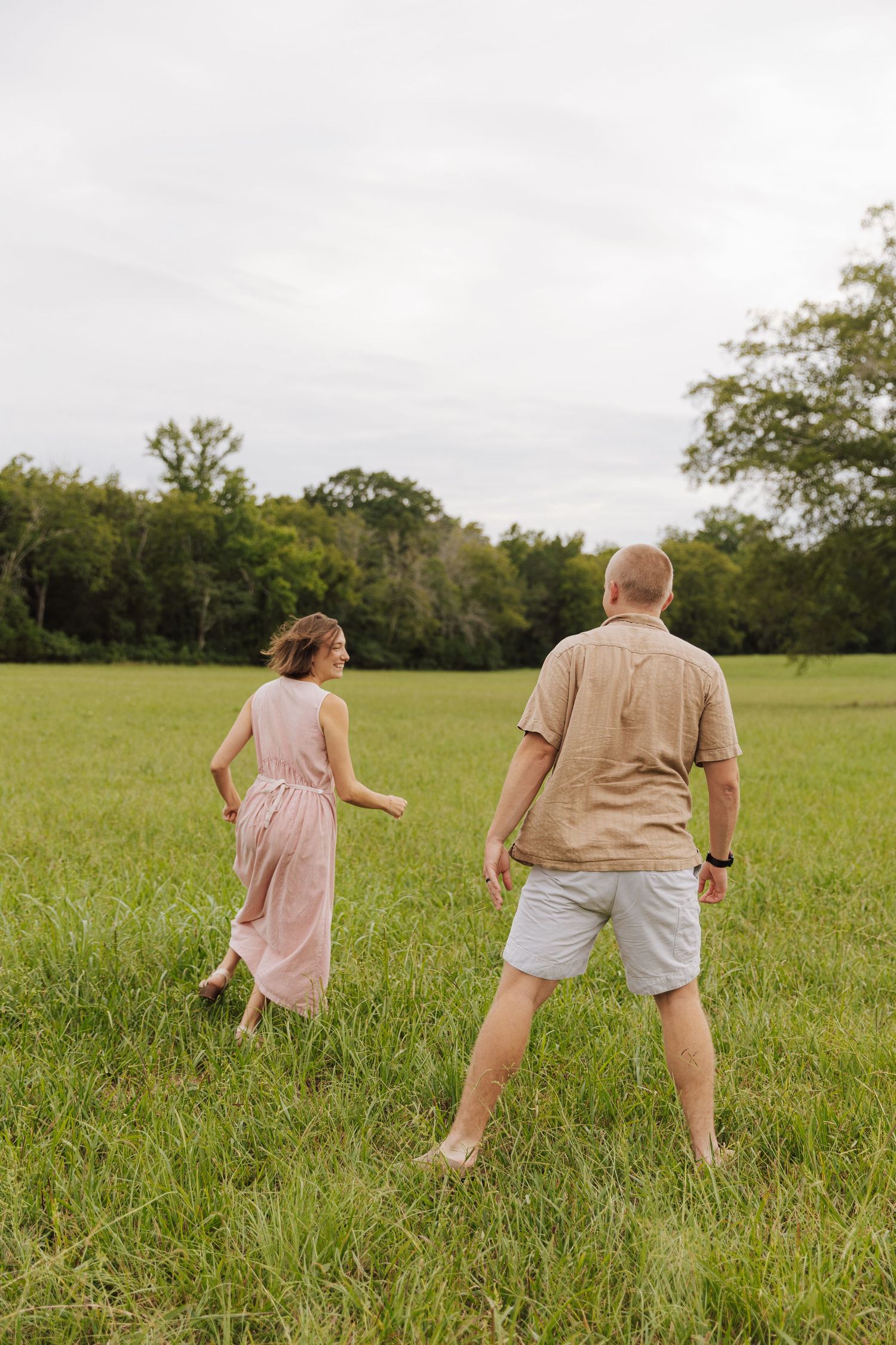 A couple walks through a green meadow on a cloudy summer day.