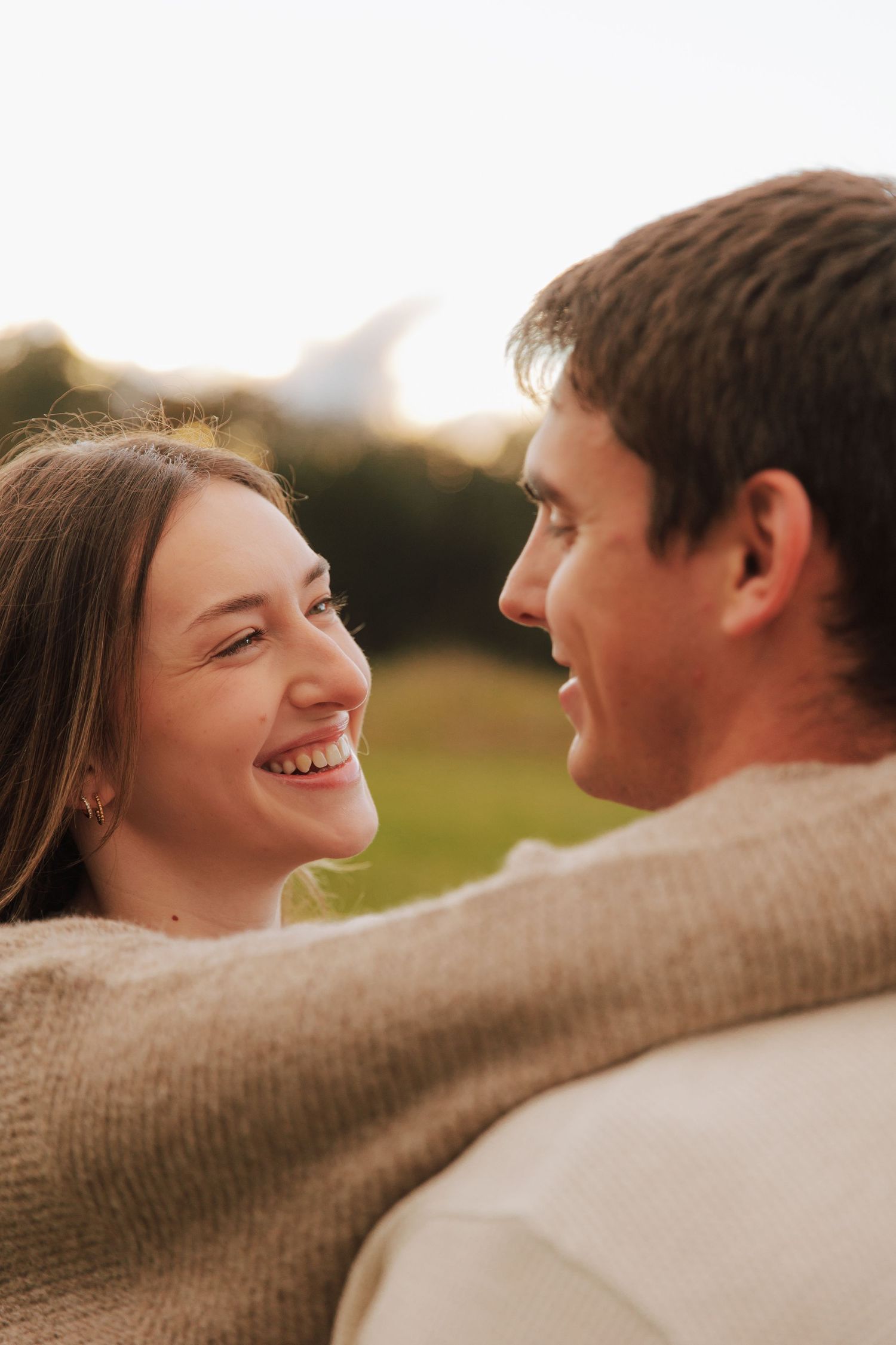 A couple sharing an intimate moment outdoors while wearing cozy sweaters at sunset.