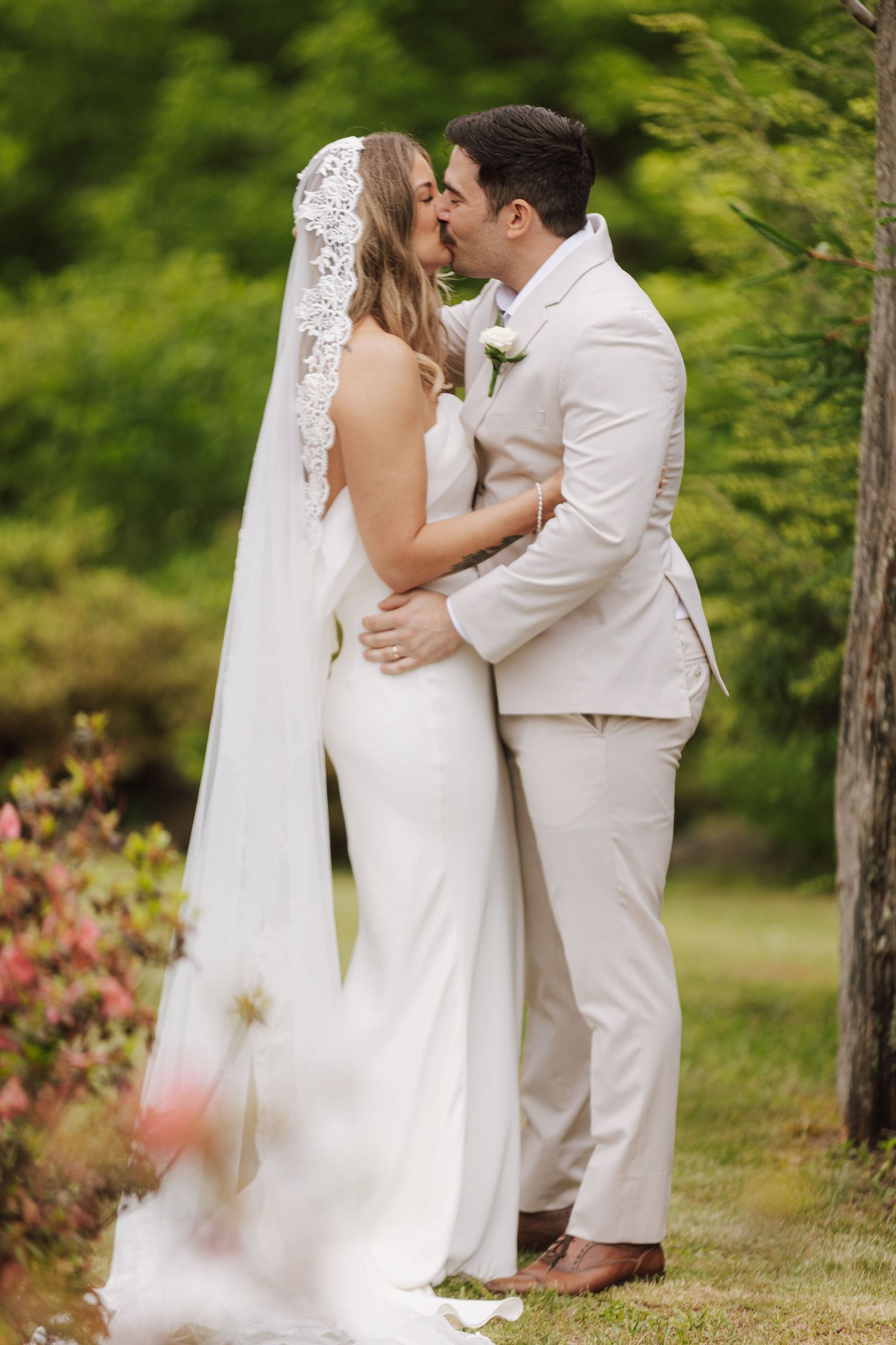 A romantic moment captured between a couple in white and cream attire against a green natural backdrop.