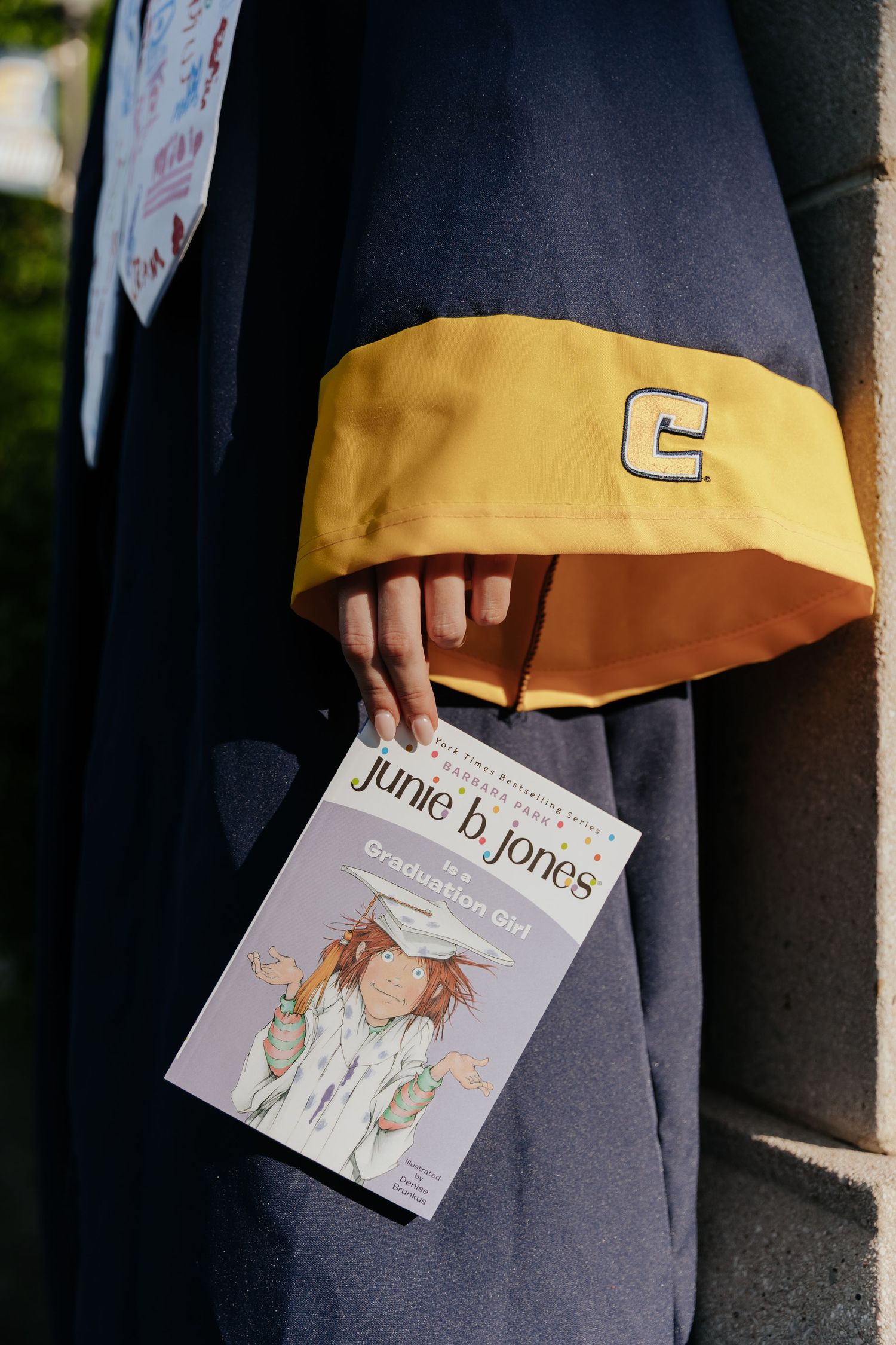A close-up series showing someone holding a children's book titled 'Junie B. Jones' against a gray and yellow outfit.