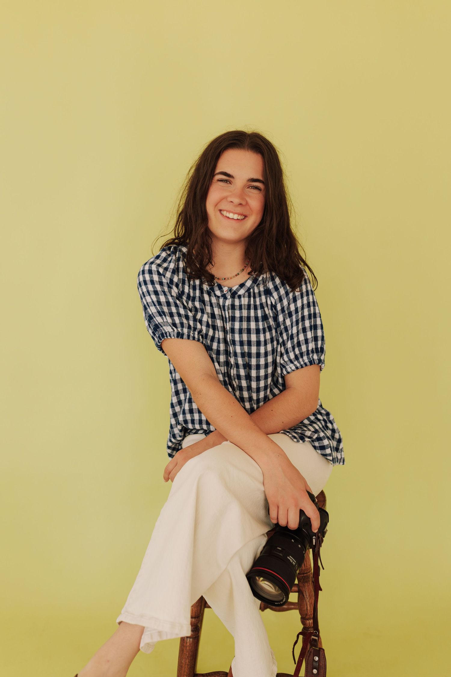 Portrait session against yellow wall wearing gingham top and white pants.