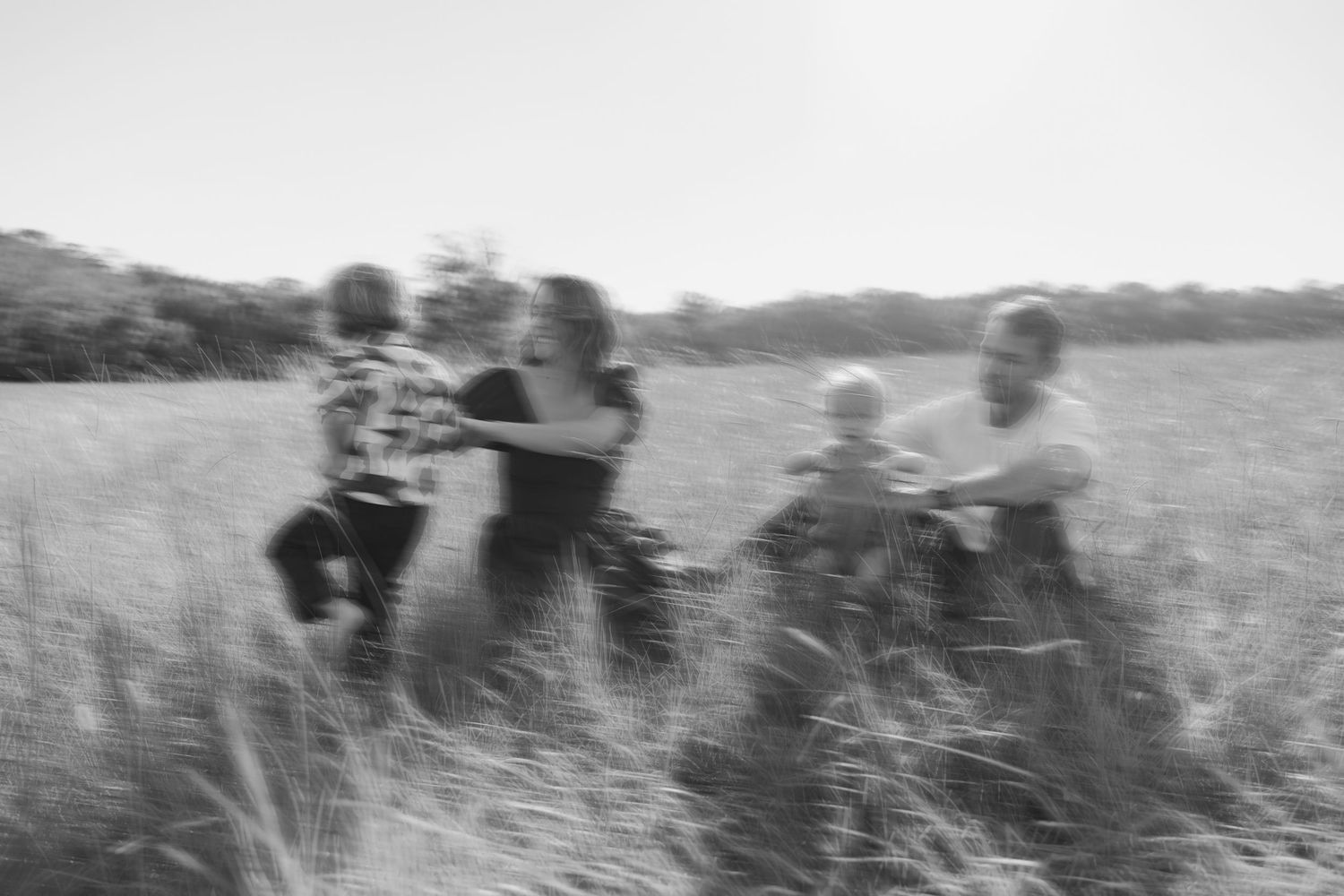 A group of people walk through tall grass in a black and white vintage photograph from a safari expedition.