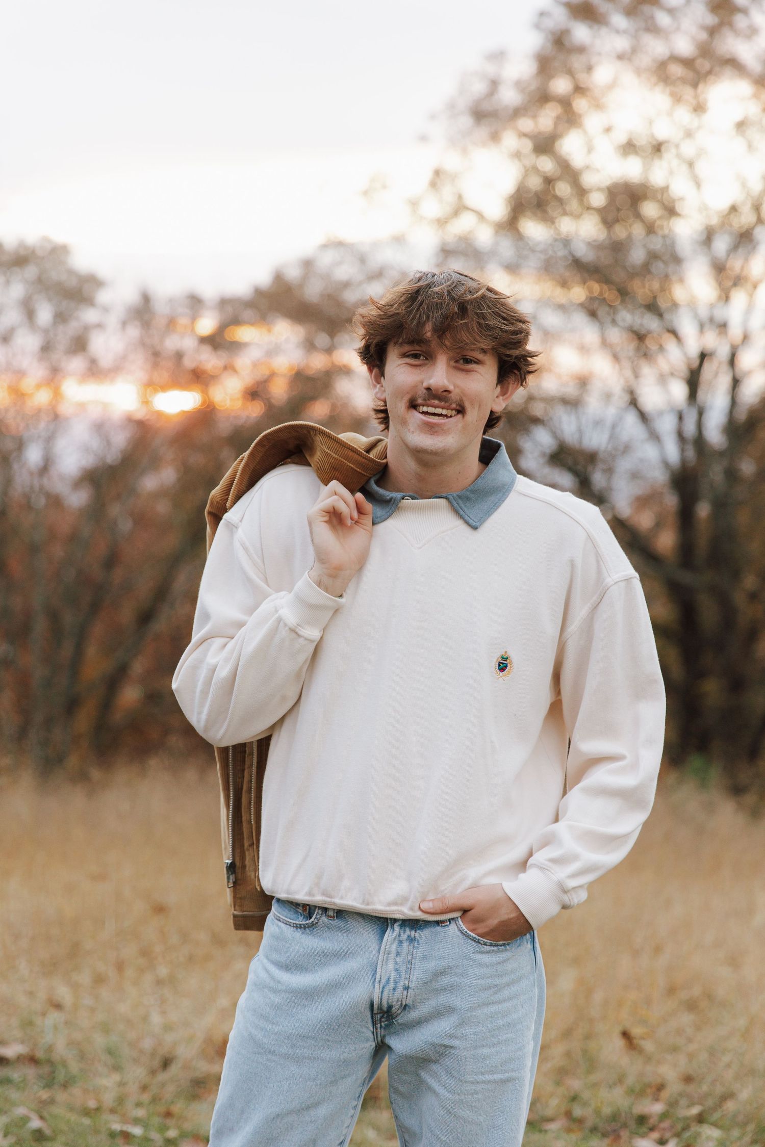 Casual outdoor portrait with person in white sweater and jeans during golden hour.