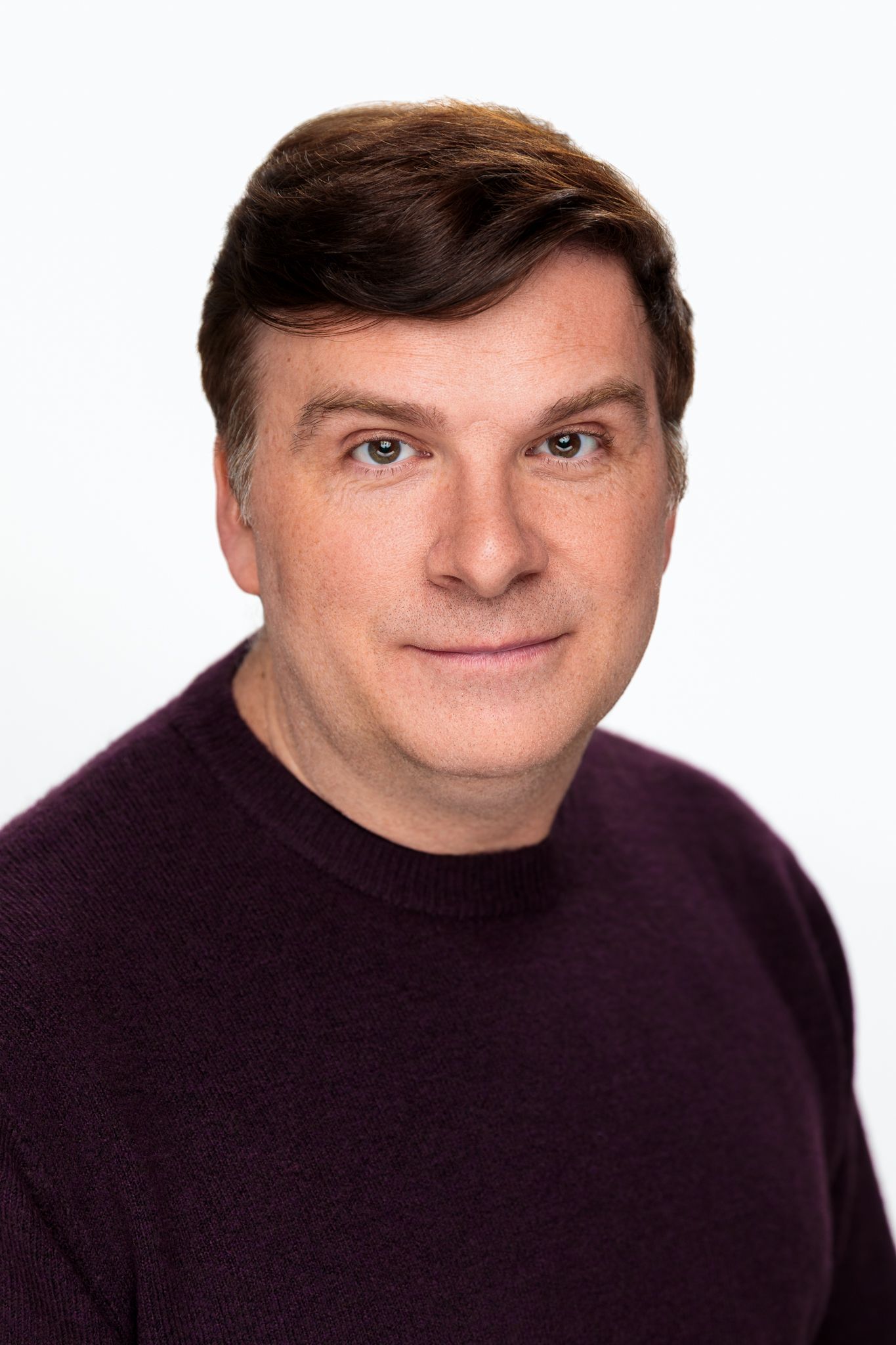 Middle-aged man in purple turtleneck sweater with subtle smile posing against white background.
