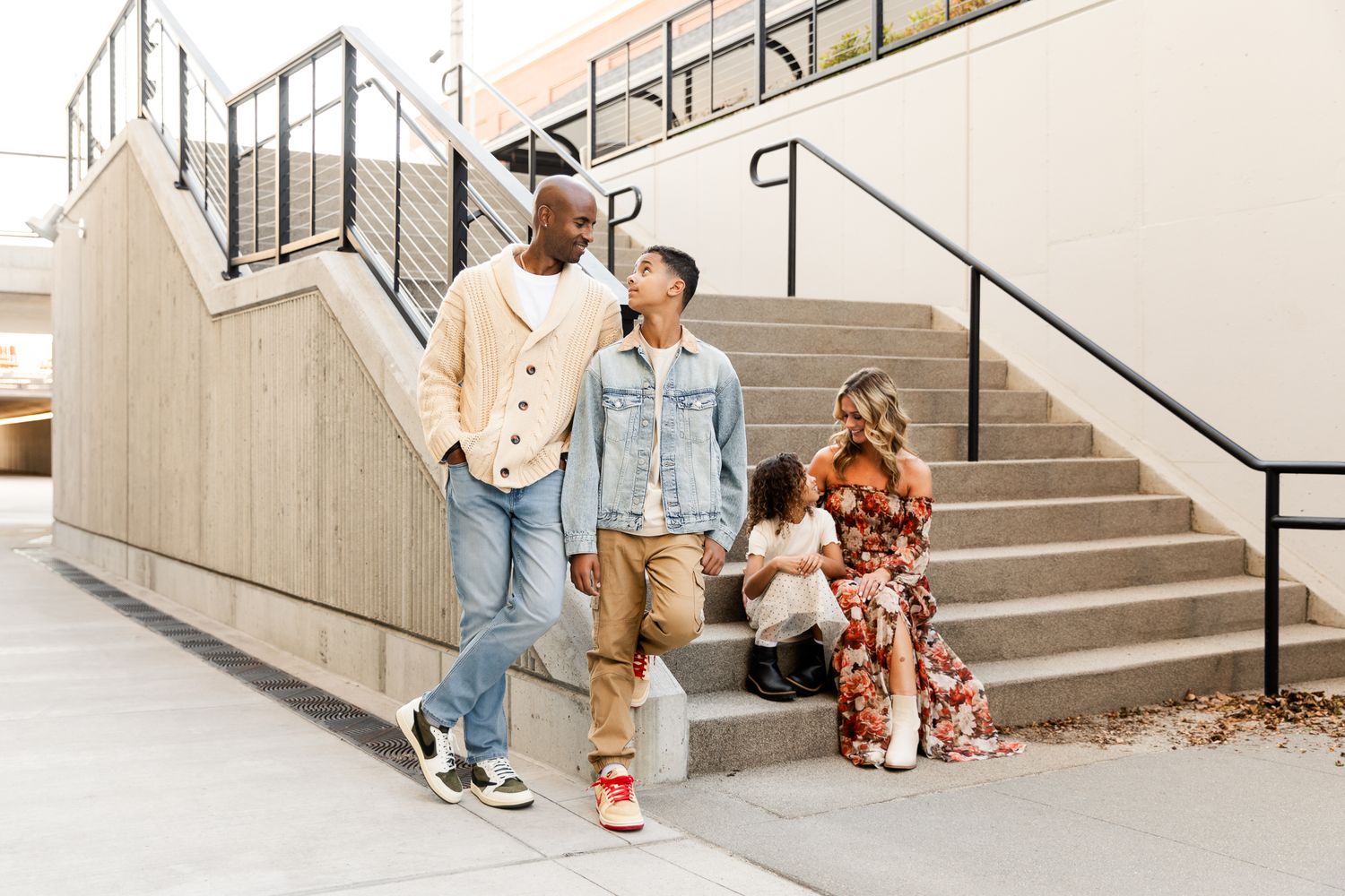 A joyful family of four walks together near outdoor stairs, with parents and two children dressed in casual stylish outfits.