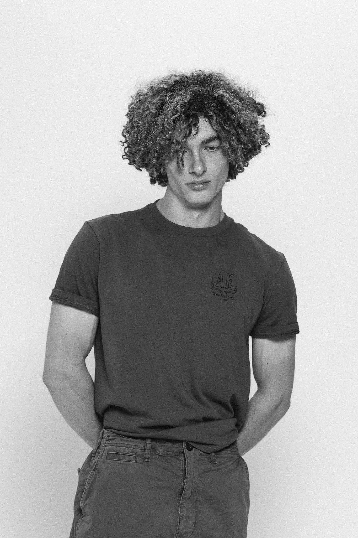 Young man with curly hair in grey t-shirt posing in black and white portrait.