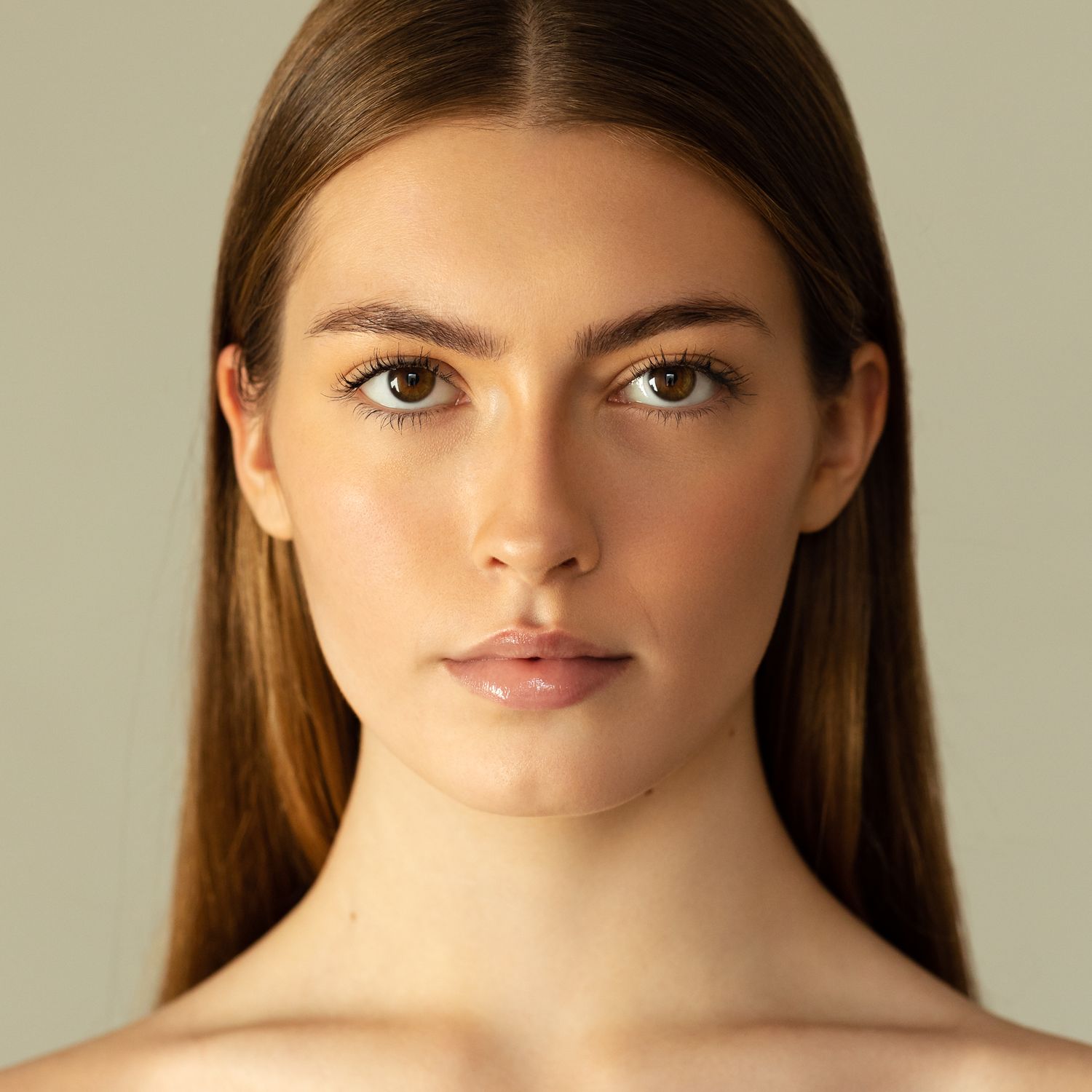 Young woman with straight brown hair and natural makeup in a clean beauty portrait on neutral background.