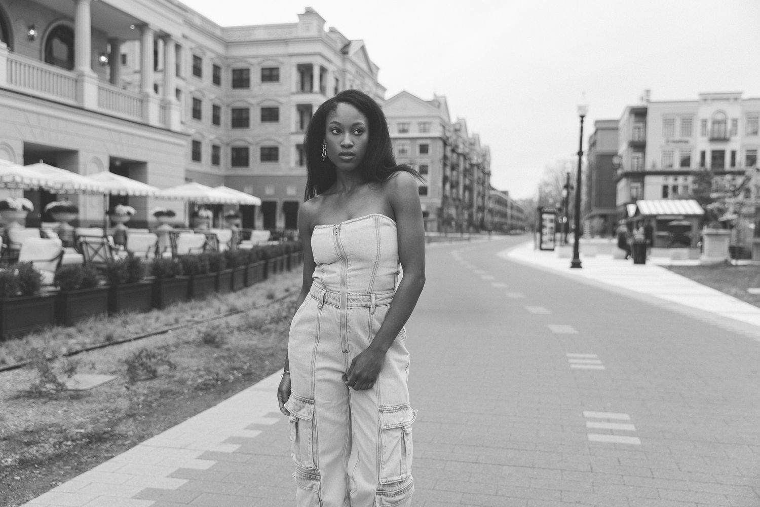 Black and white photo of a young woman in cargo pants and tube top posing on an empty urban street.