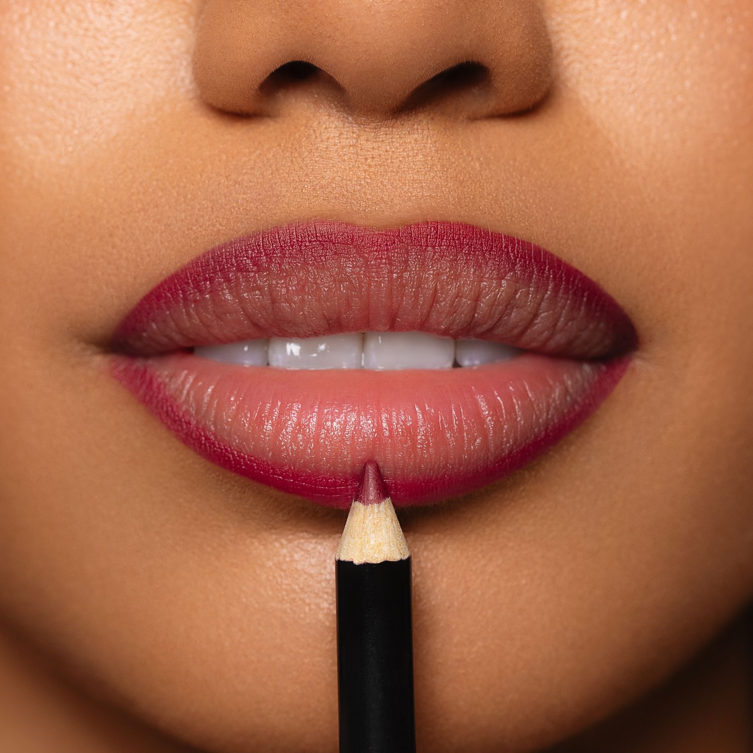 Close-up of deep berry lip liner pencil being applied to full lips with rich magenta lipstick.