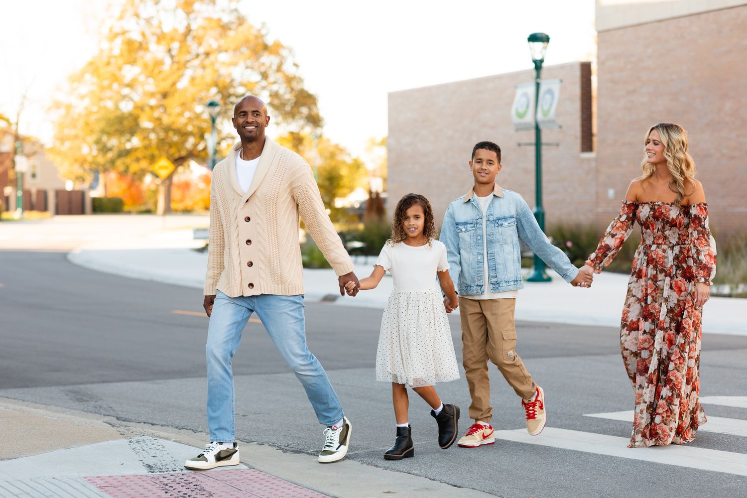 Family of four crossing street holding hands in urban setting during golden hour autumn session.