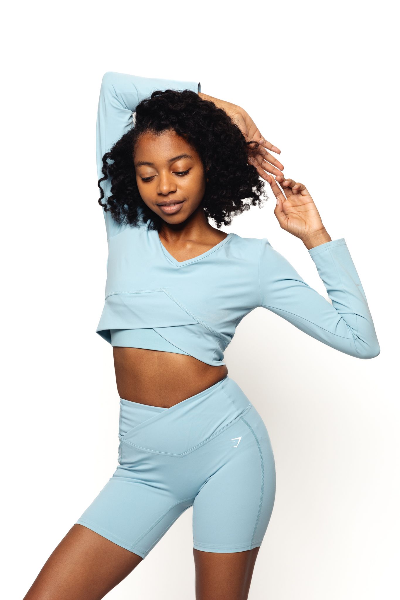 Black woman in light blue athletic crop top and shorts posing against white background.