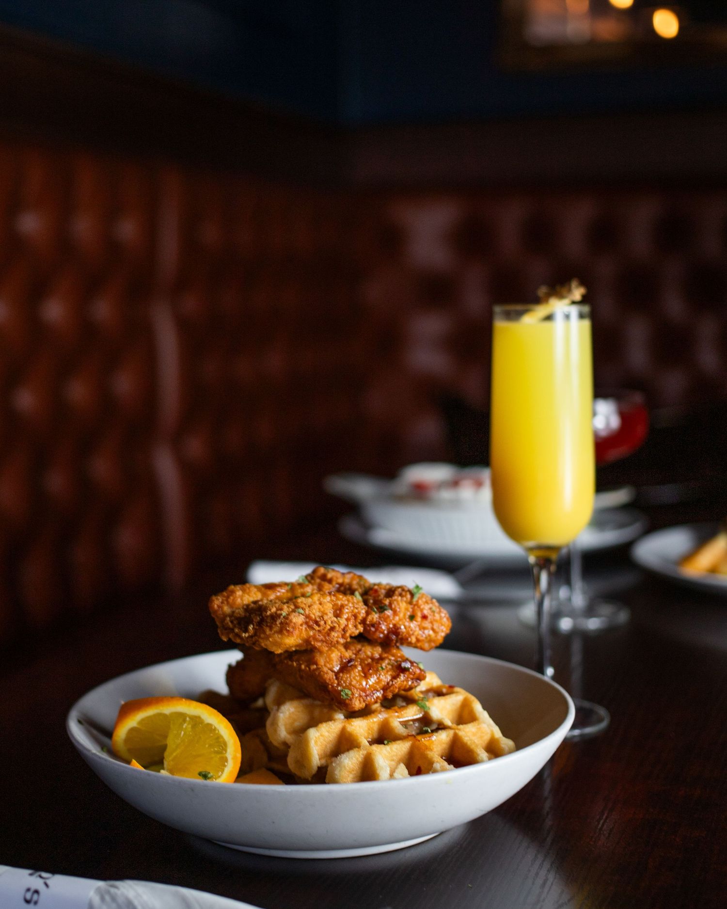 A plate of fried chicken and waffles, accompanied by a glass of orange juice, on a wooden table.